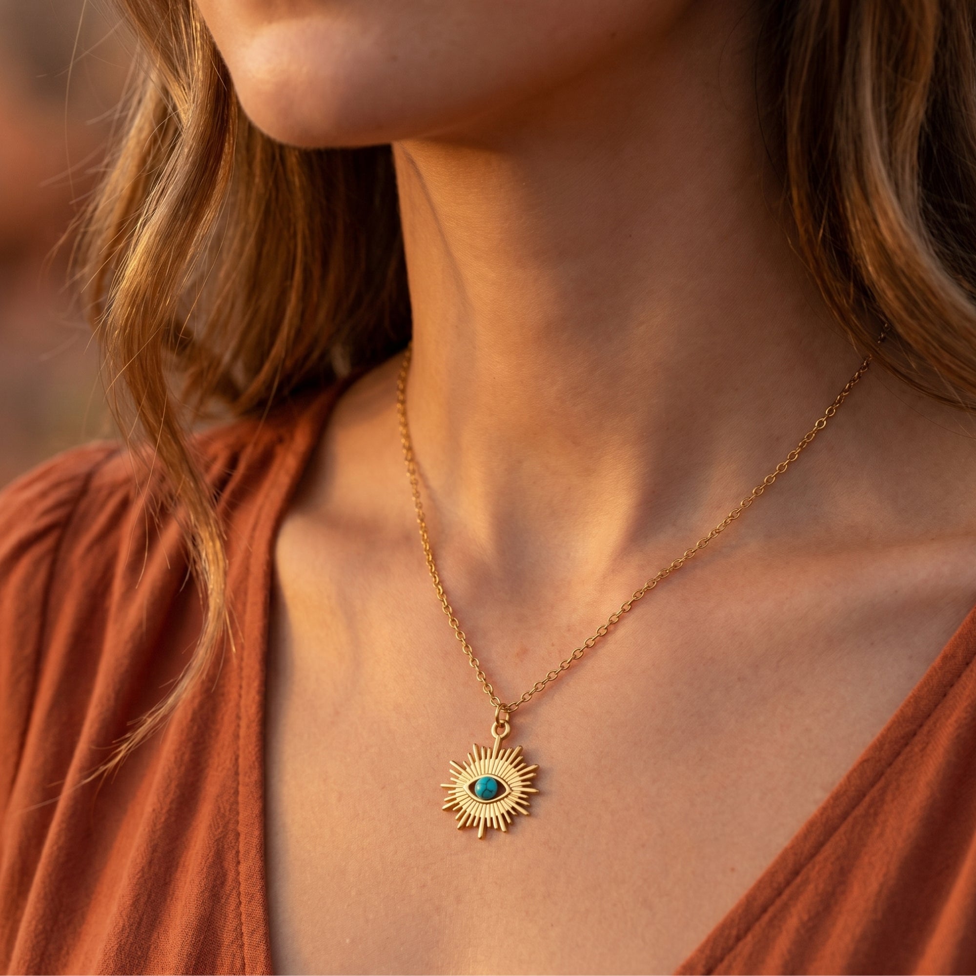Gold finish turquoise pendant necklace worn by a model against a rust-colored top for a bohemian look.