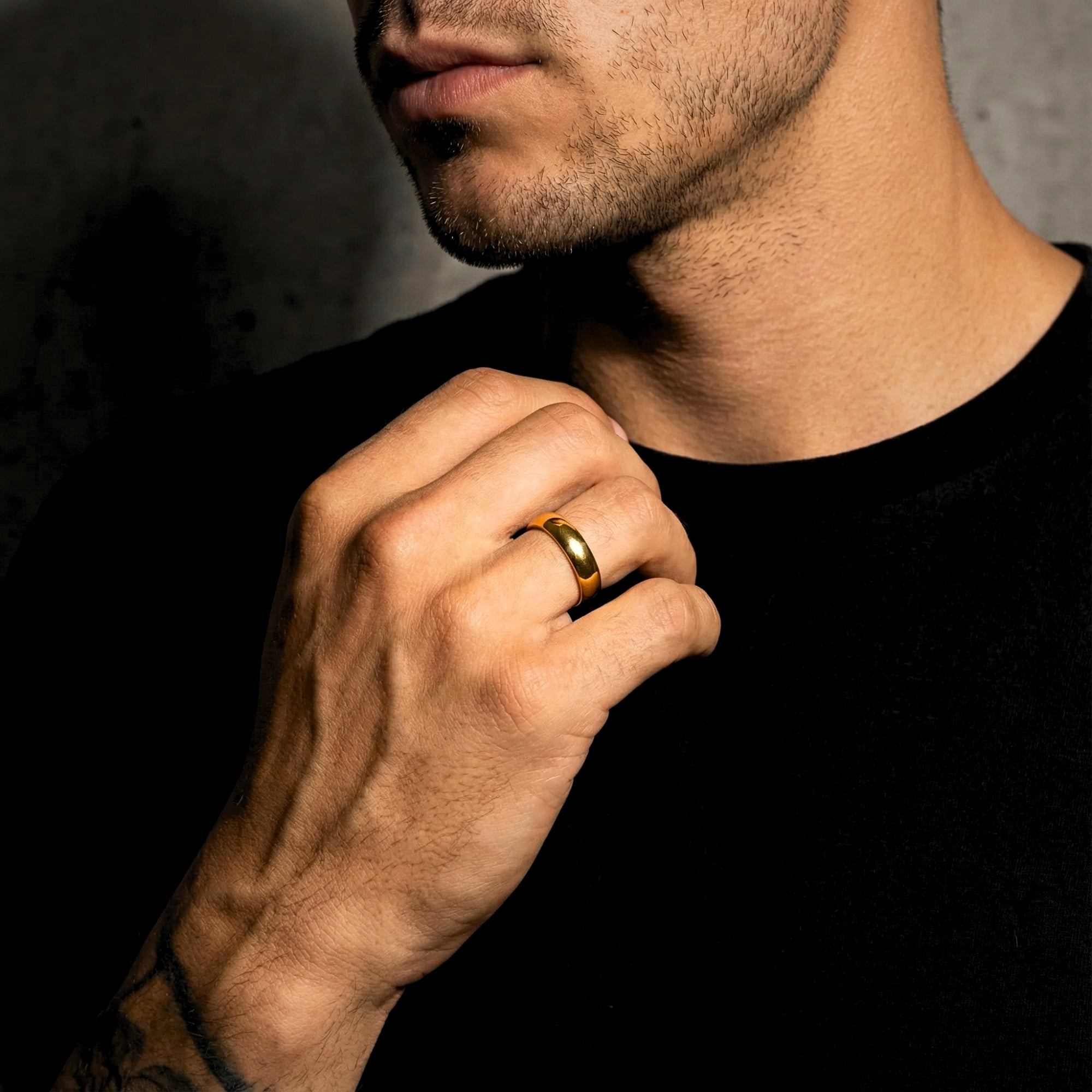 Men's gold tone stainless steel band ring worn on a model's hand against a dark background.