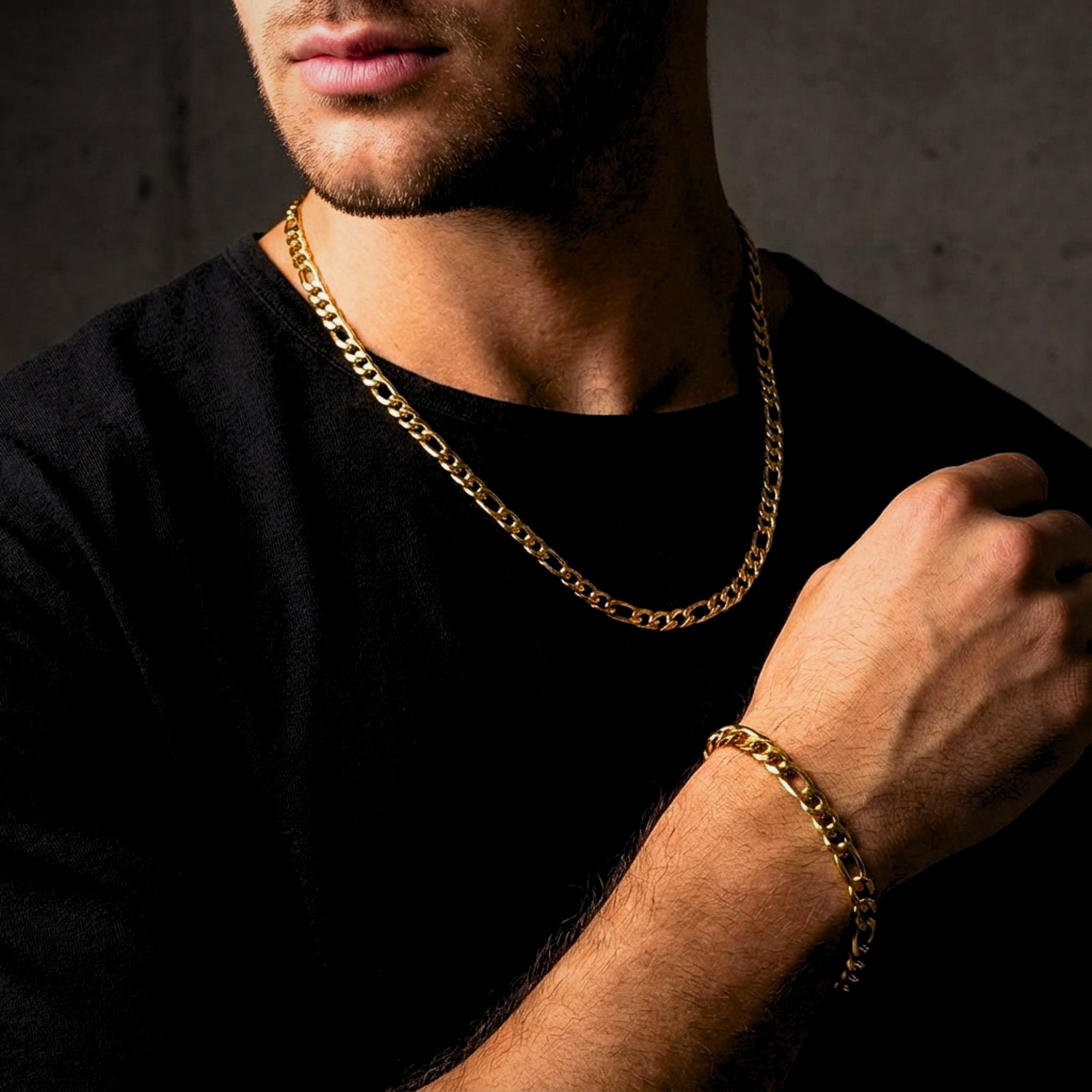 Man wearing a gold Figaro chain necklace and matching bracelet over a black t-shirt for a masculine style.