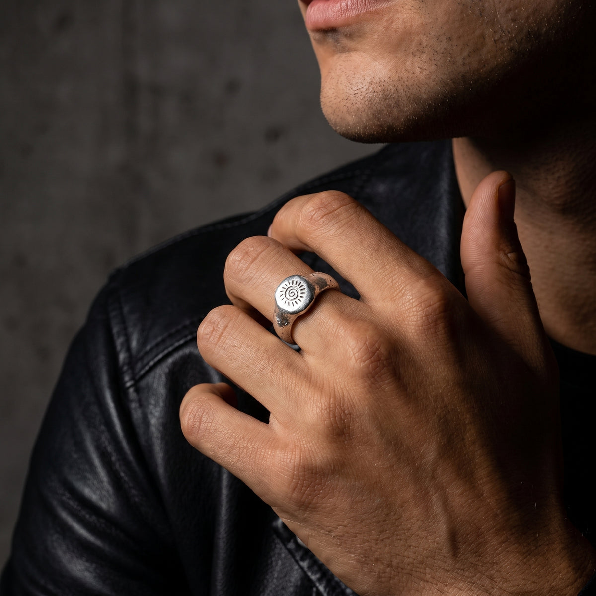 Model wearing the silver solar spiral signet ring near his chin with a black leather jacket visible.