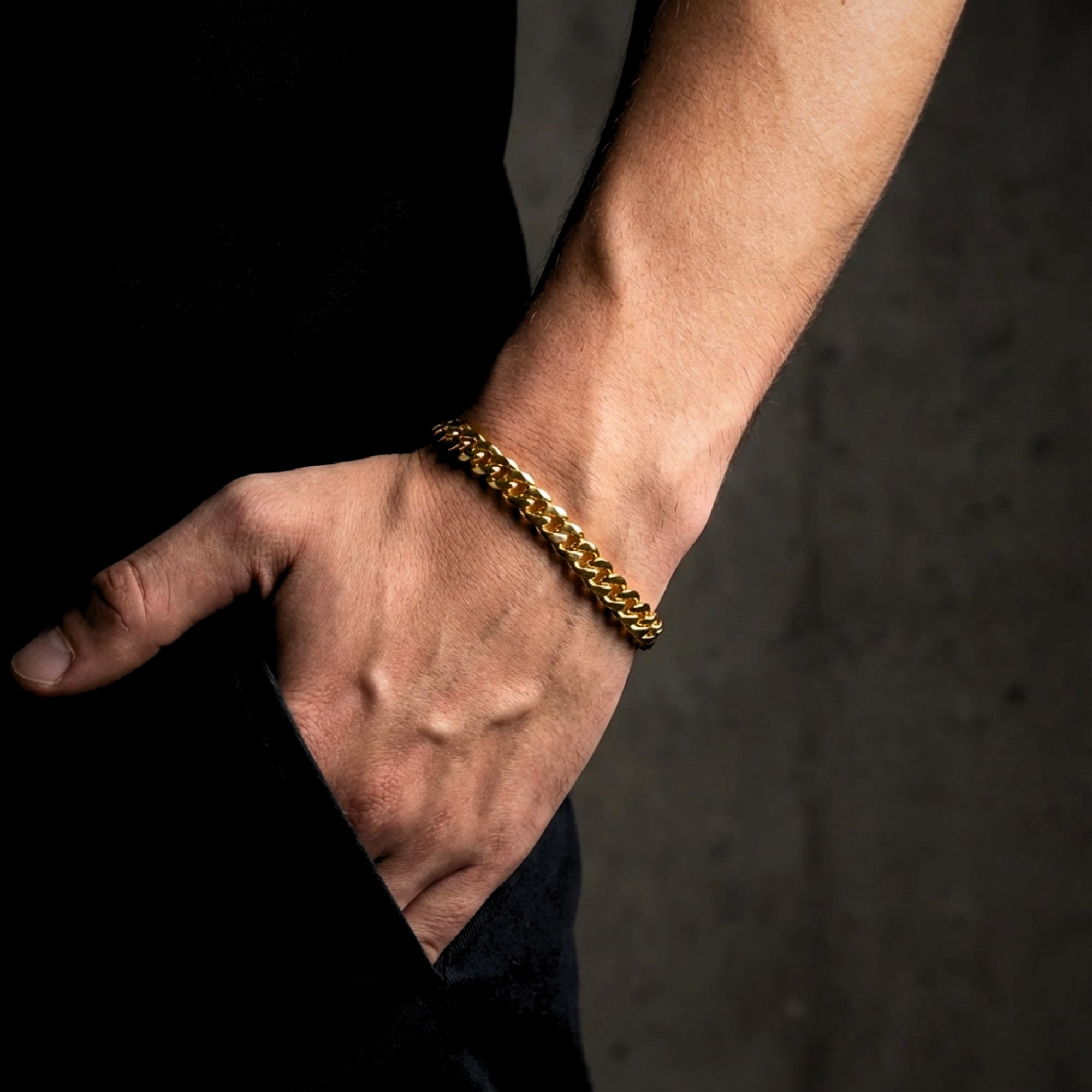 Gold stainless steel Cuban link bracelet worn on a man's wrist with hand in pocket.