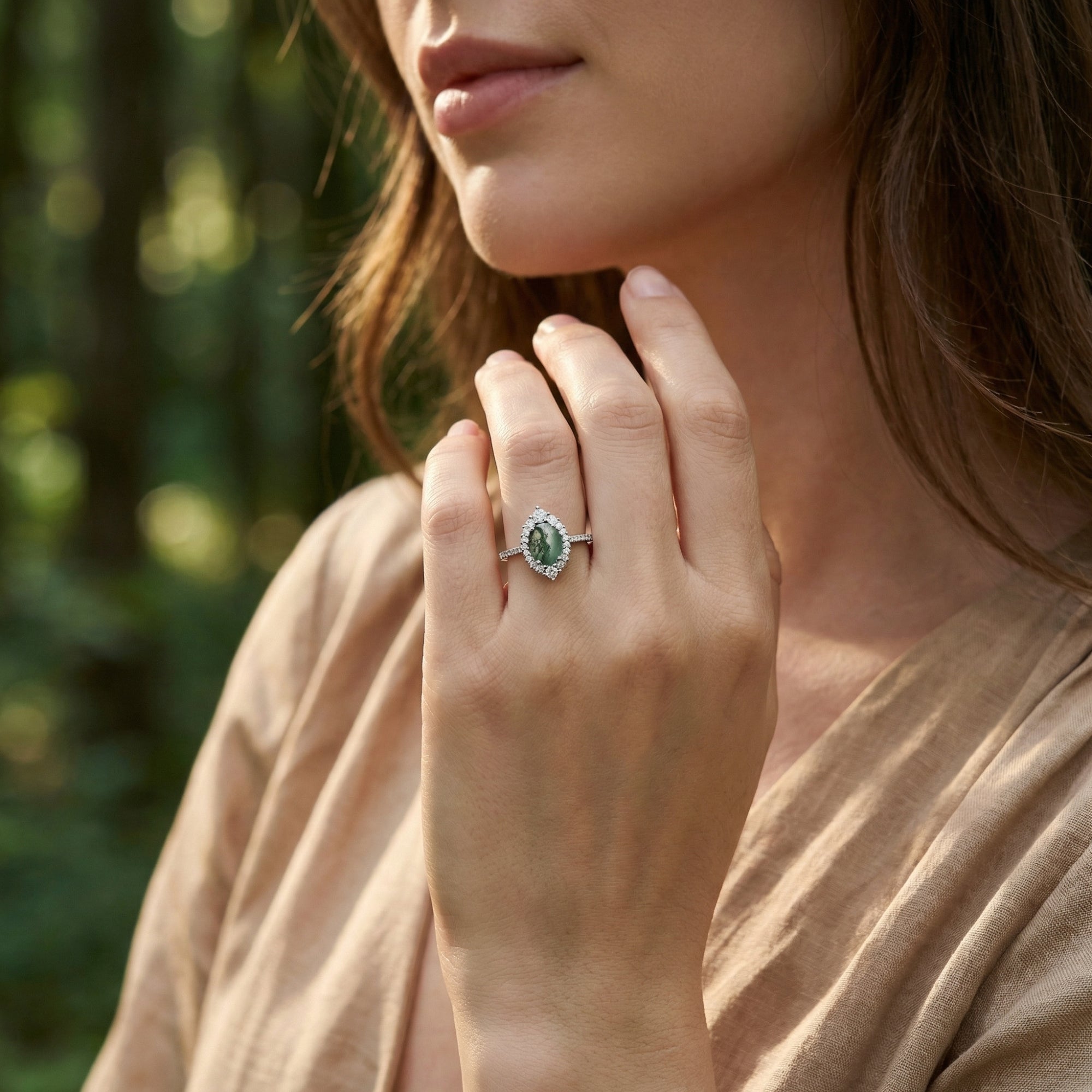 Model wearing an oval moss agate sterling silver halo ring on her finger, paired with a beige linen outfit.