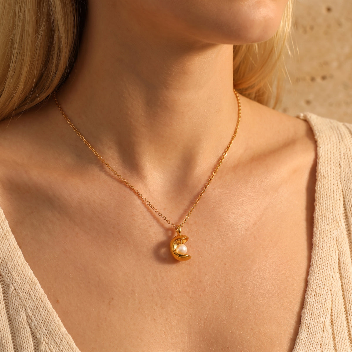 Model wearing the gold-tone crescent pearl necklace with a V-neck knit top.