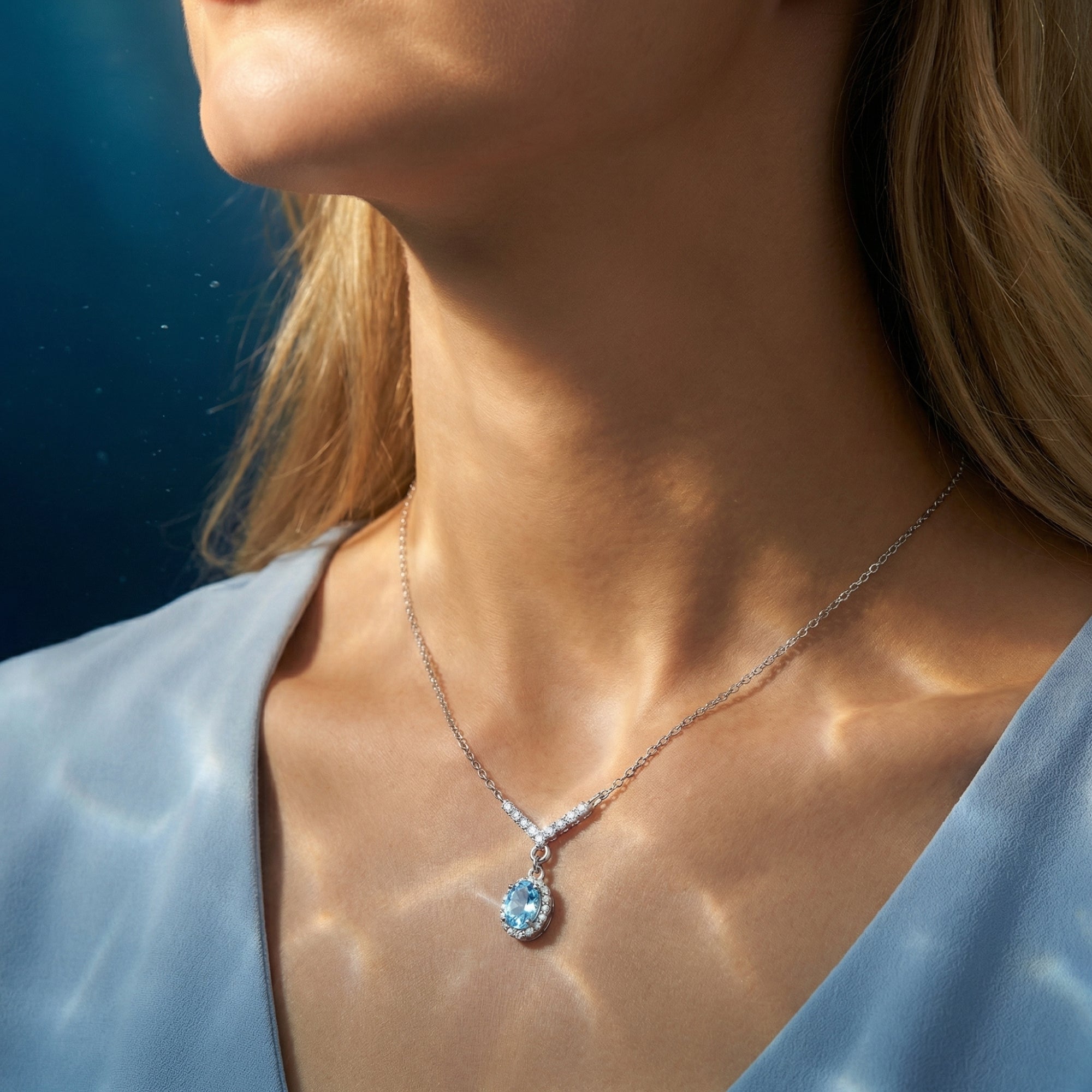 Model wearing the Lyrissa oval aquamarine halo necklace in white gold with a V-shaped diamond-accented chain.