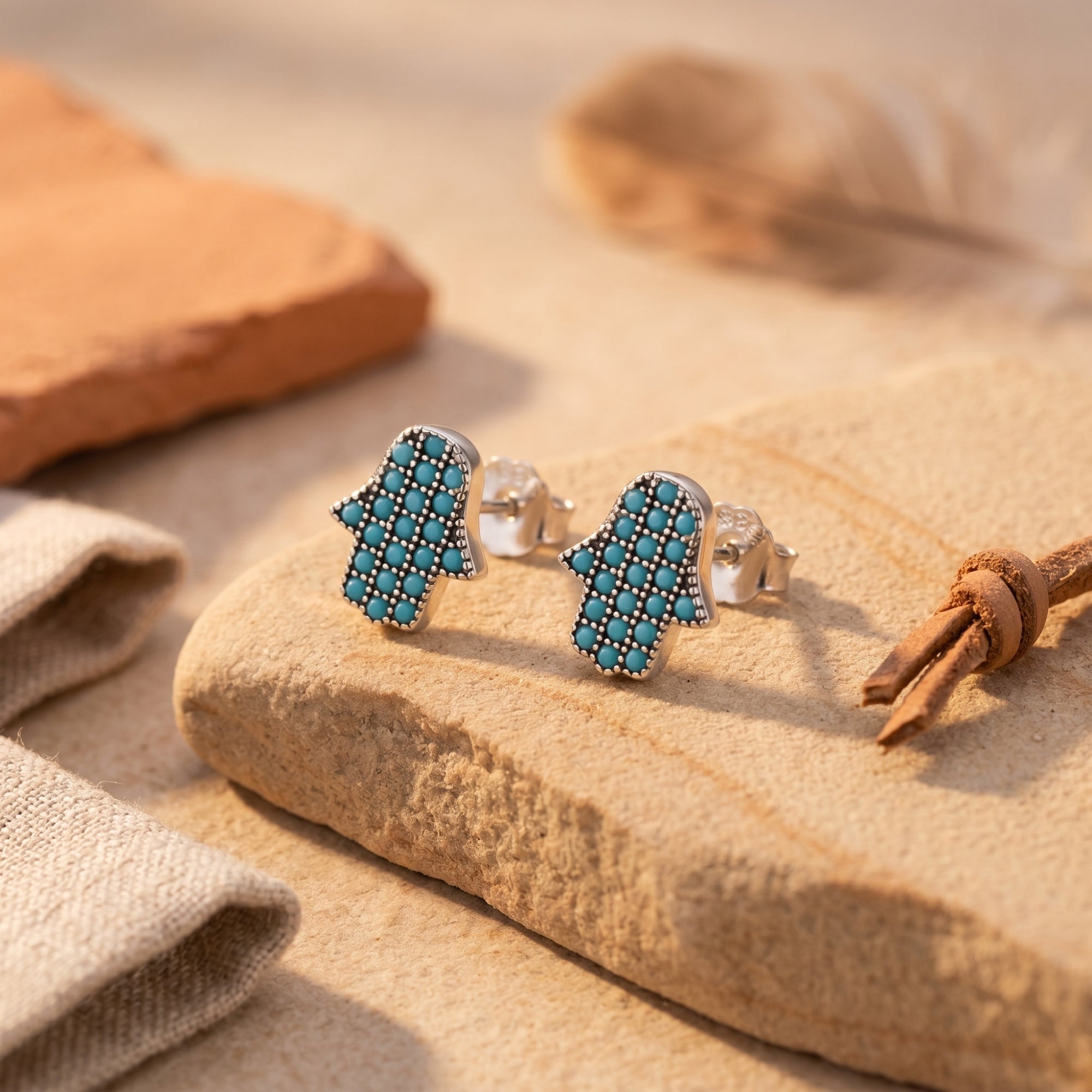 Close-up of silver Hamsa hand earrings featuring round turquoise stones on a textured stone surface.