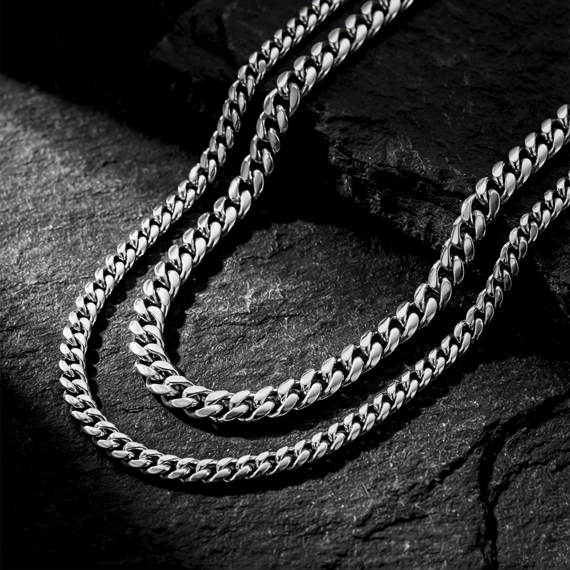 Close-up of the polished silver stainless steel links on the Cuban Duo stacked necklace set over dark stone.