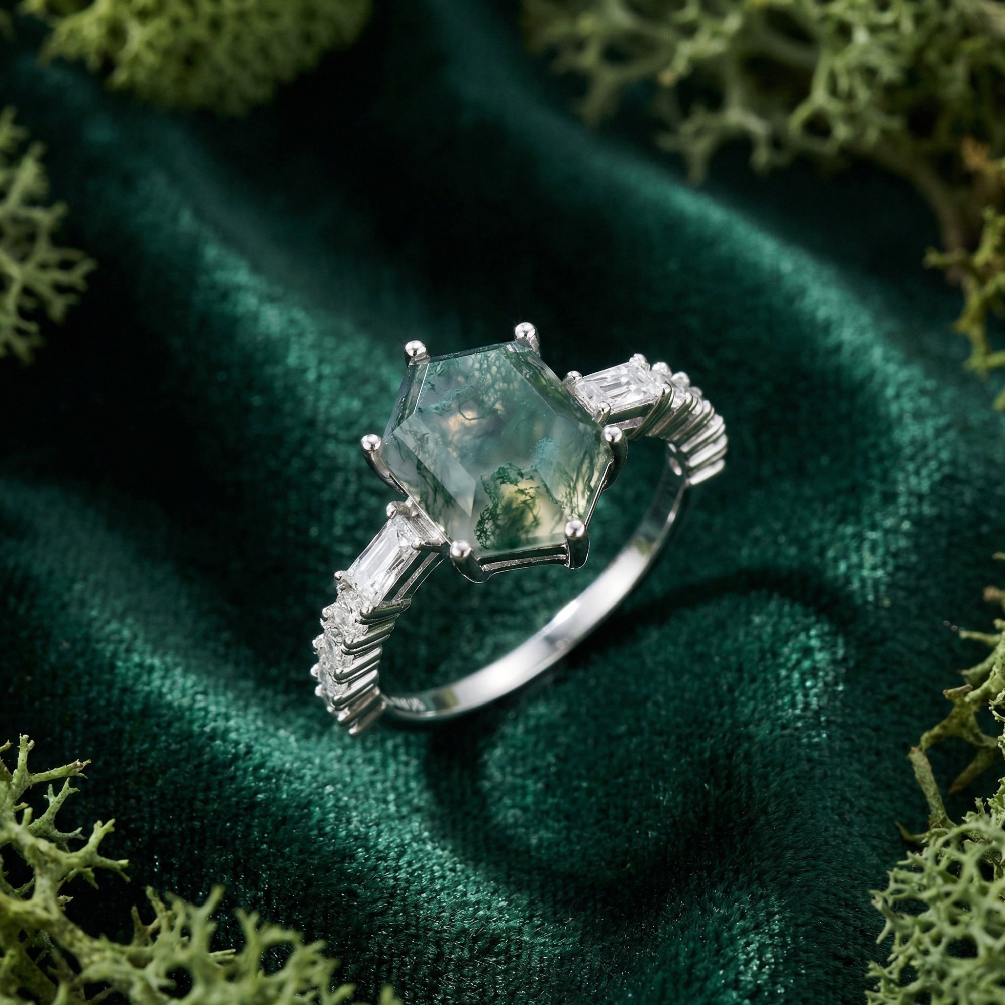 Side view of a hexagonal moss agate ring with baguette accents in sterling silver on green velvet.