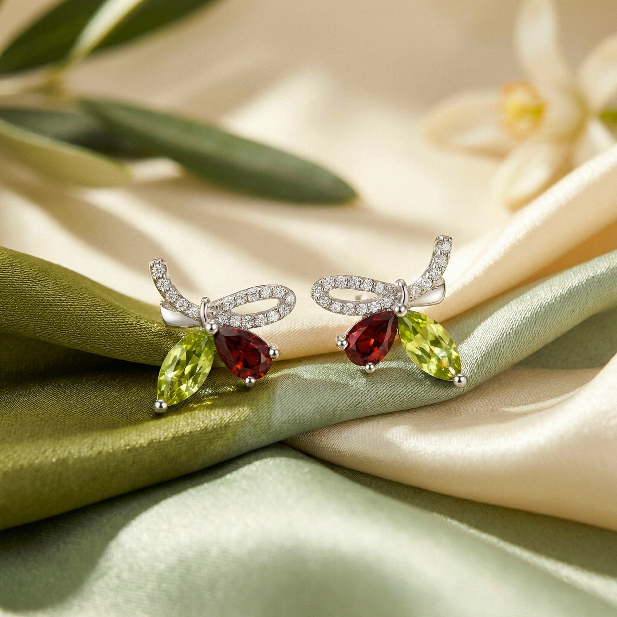 Macro shot of Giselle Marquise sterling silver bow earrings with marquise peridot and red stones on draped silk fabric.