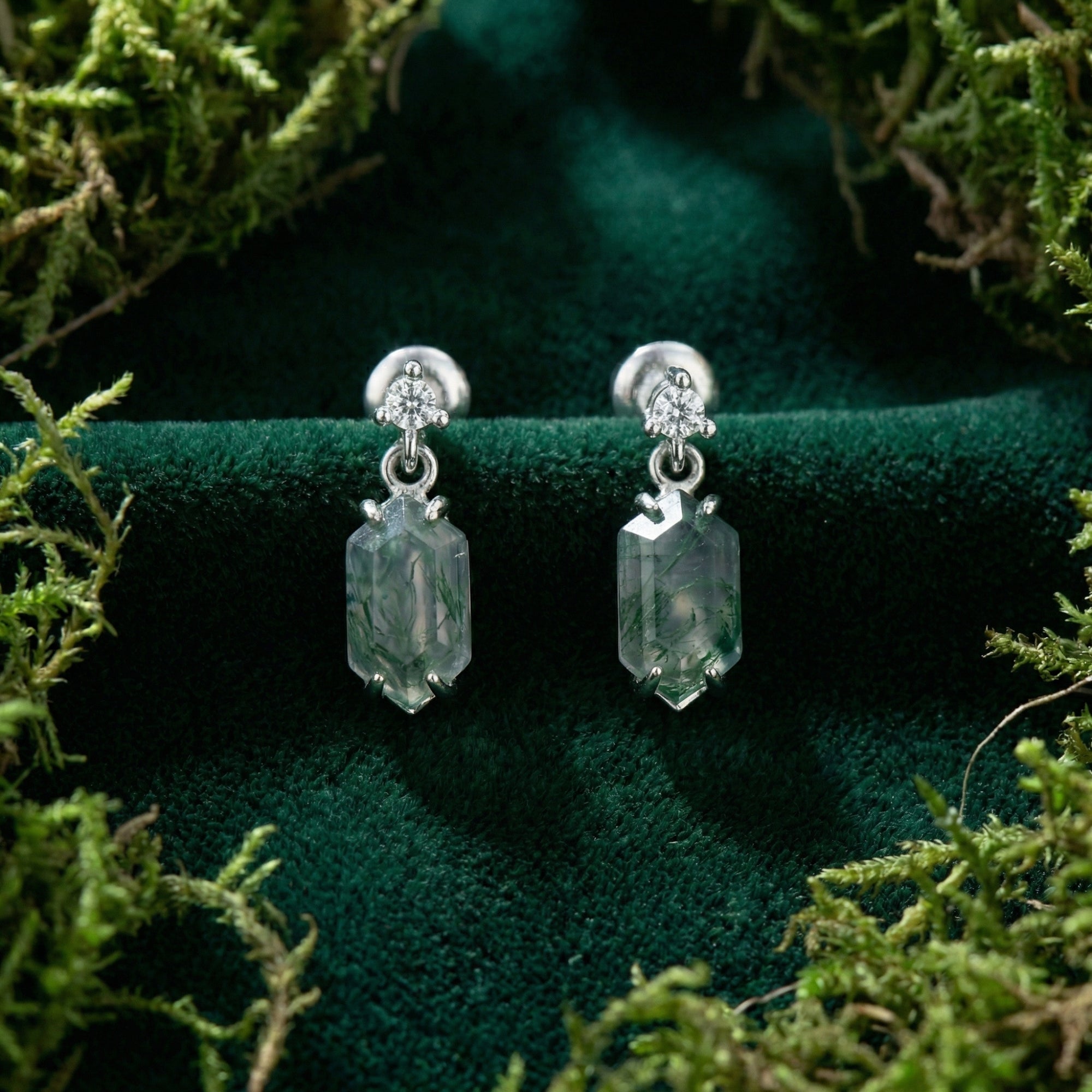 Front view of barrel cut moss agate earrings in S925 sterling silver displayed on green velvet and moss.