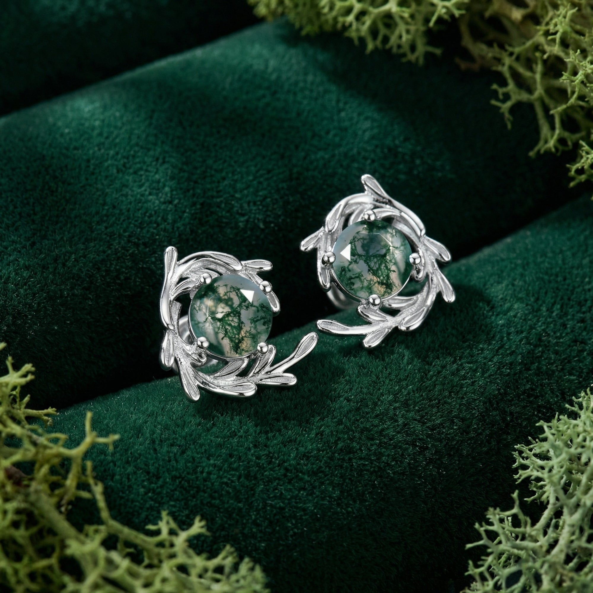 Close-up of sterling silver vine wrap stud earrings featuring round natural moss agate stones on green velvet.