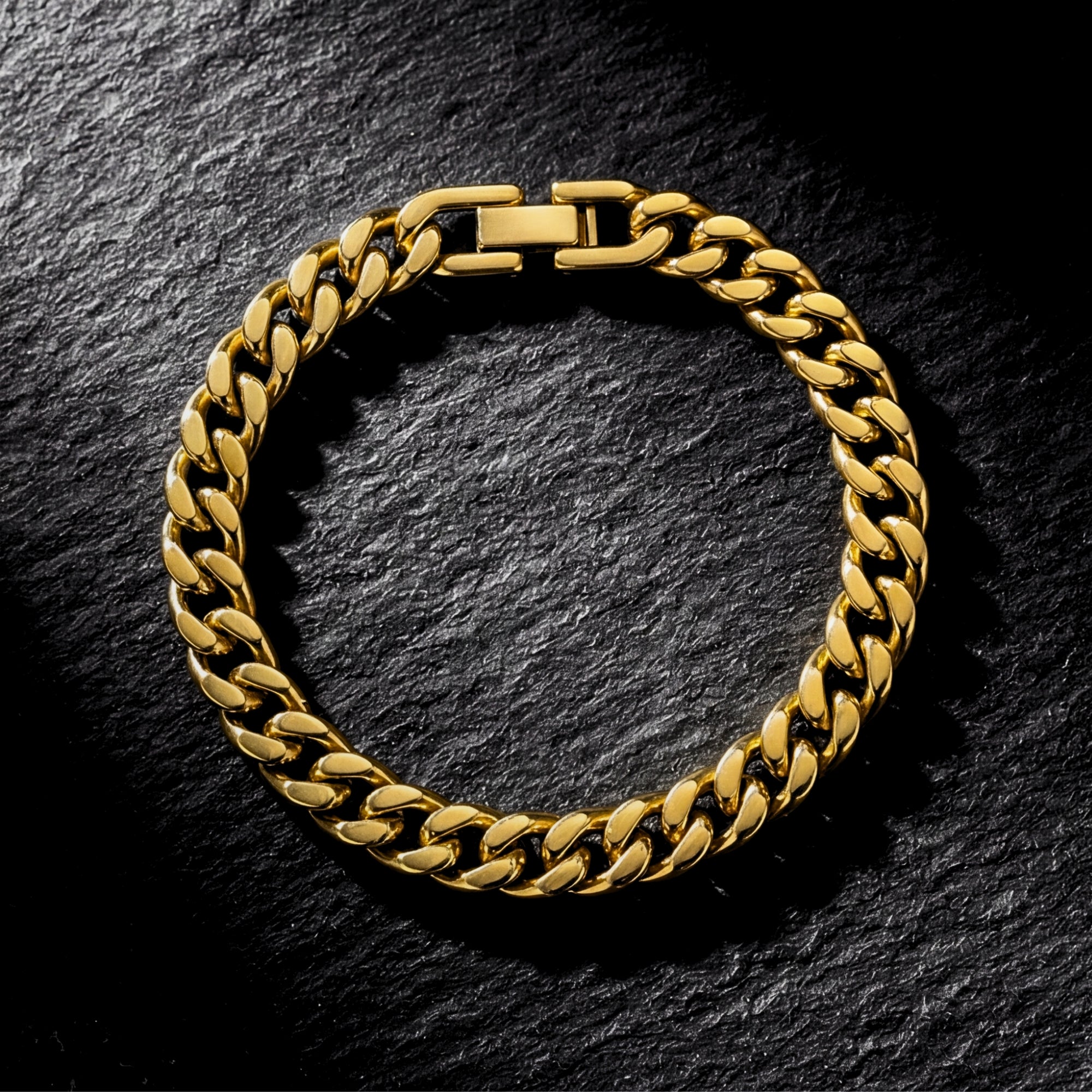 Top-down view of a gold stainless steel Cuban link bracelet on a dark textured stone background.