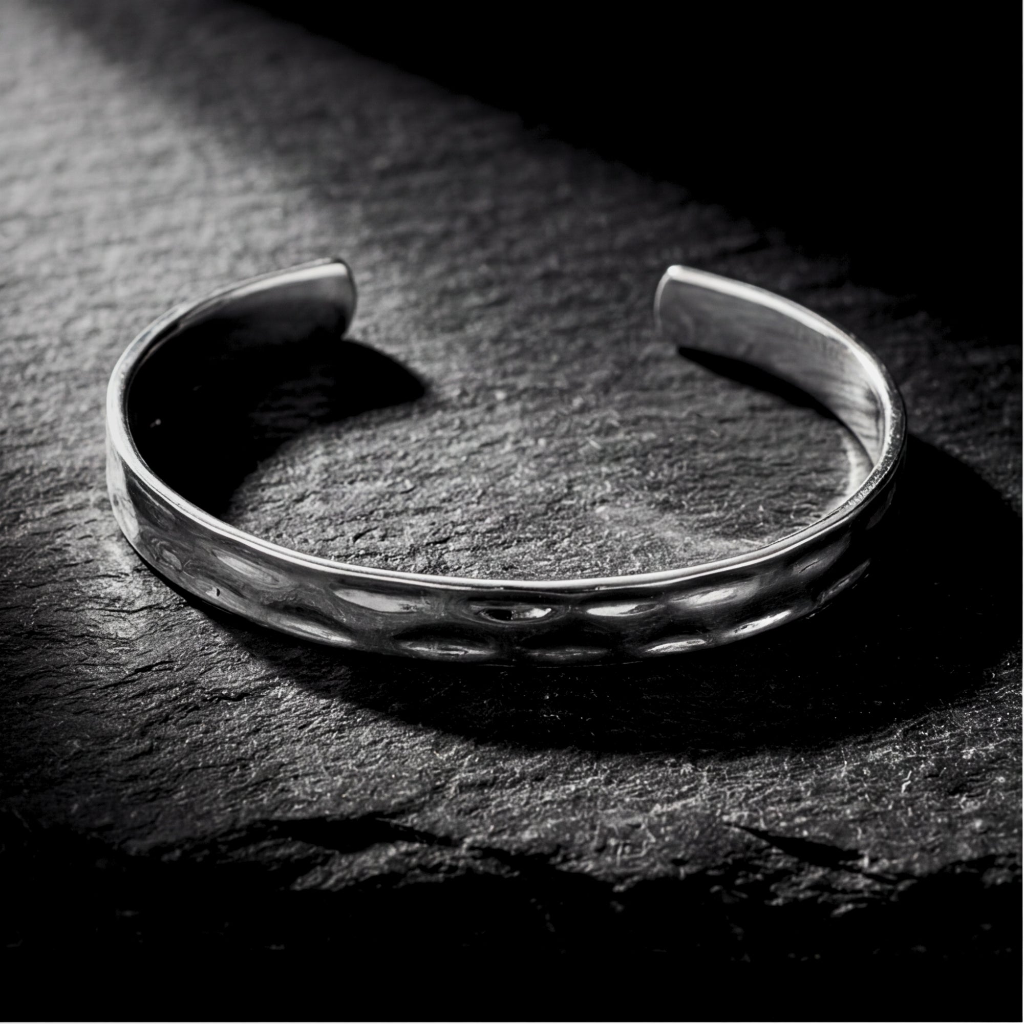 Silver hammered stainless steel cuff bangle resting flat on a dark slate background.