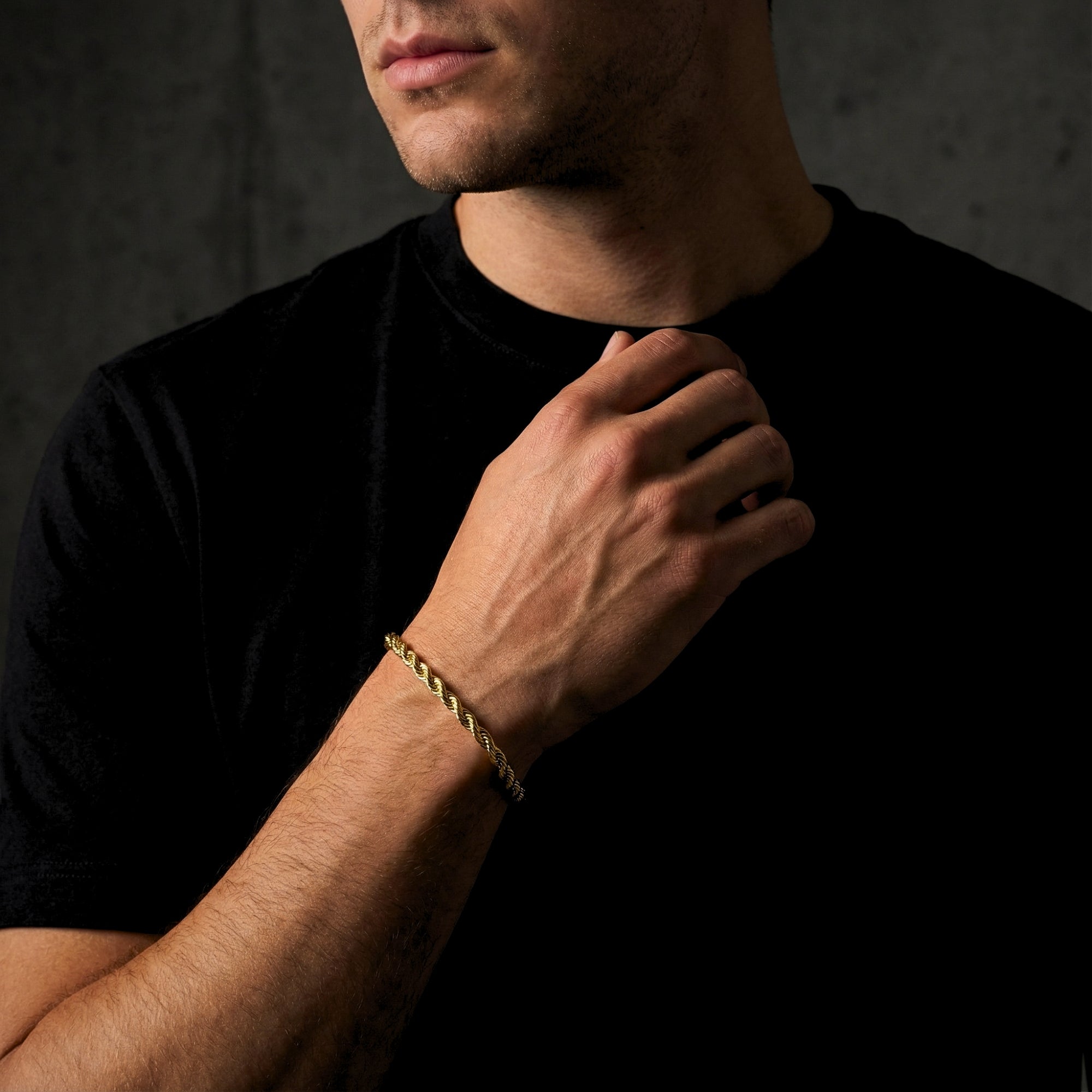 Men's gold rope bracelet worn on a wrist, styled with a black t-shirt for a classic look.