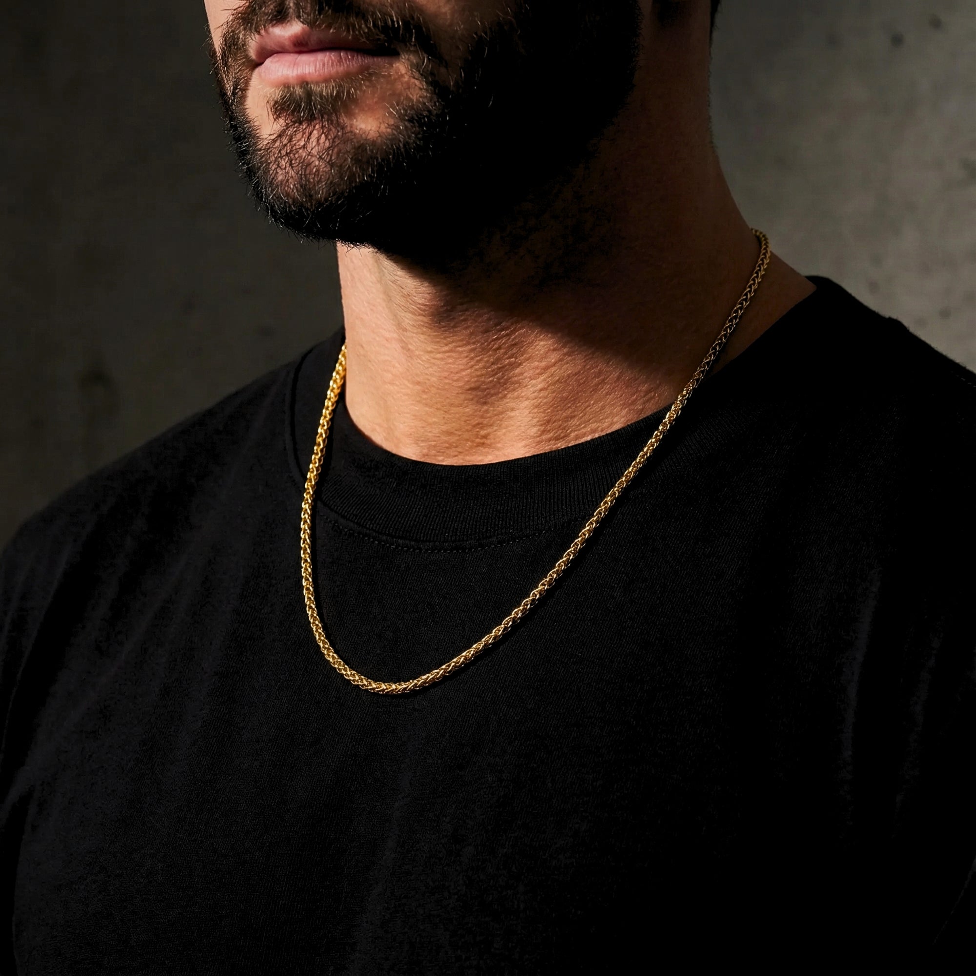 Men's gold stainless steel wheat chain necklace styled with a black shirt.