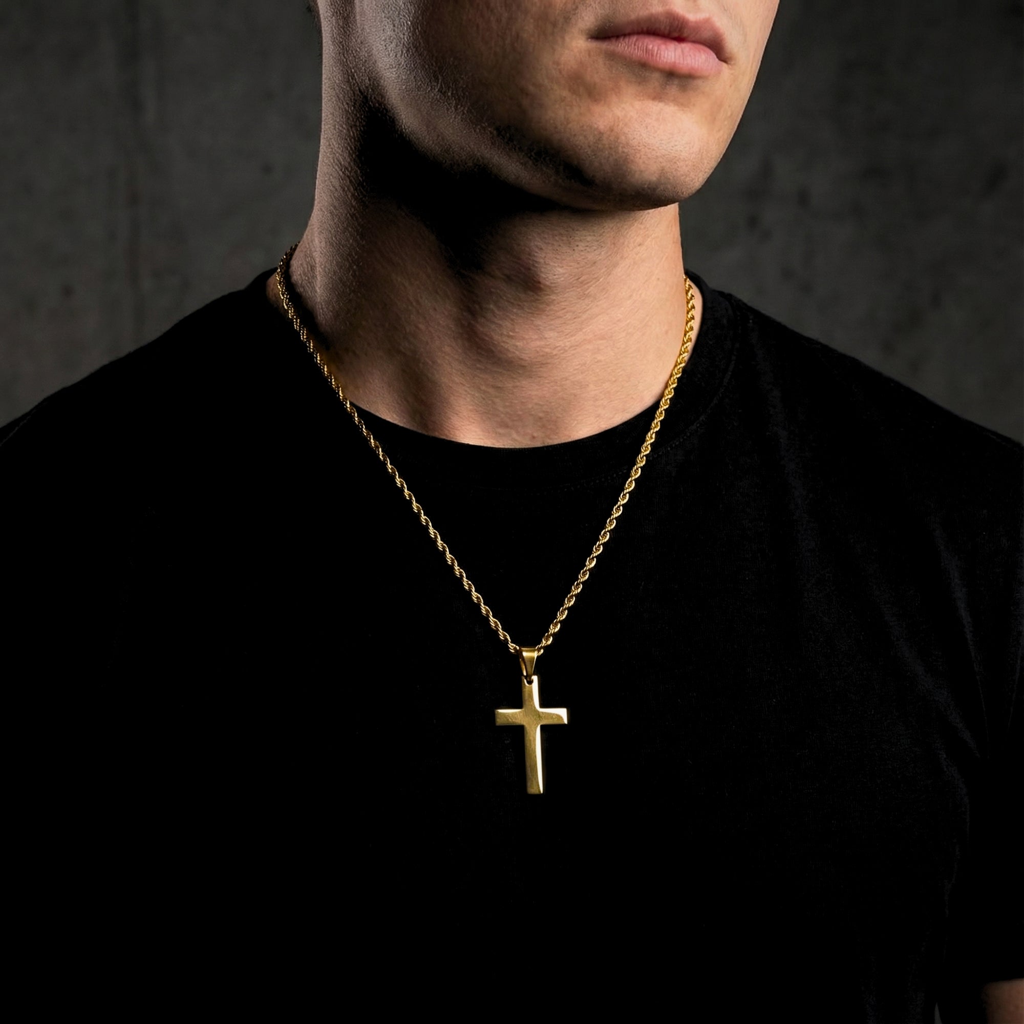 Front view of a man wearing the gold Apostle Cross pendant on a rope chain over a black t-shirt.