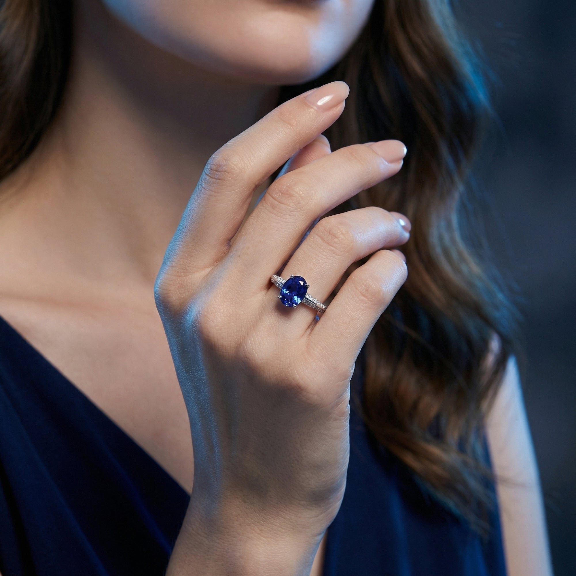 Sterling silver ring with an oval natural tanzanite center stone worn on a model's finger in soft lighting.