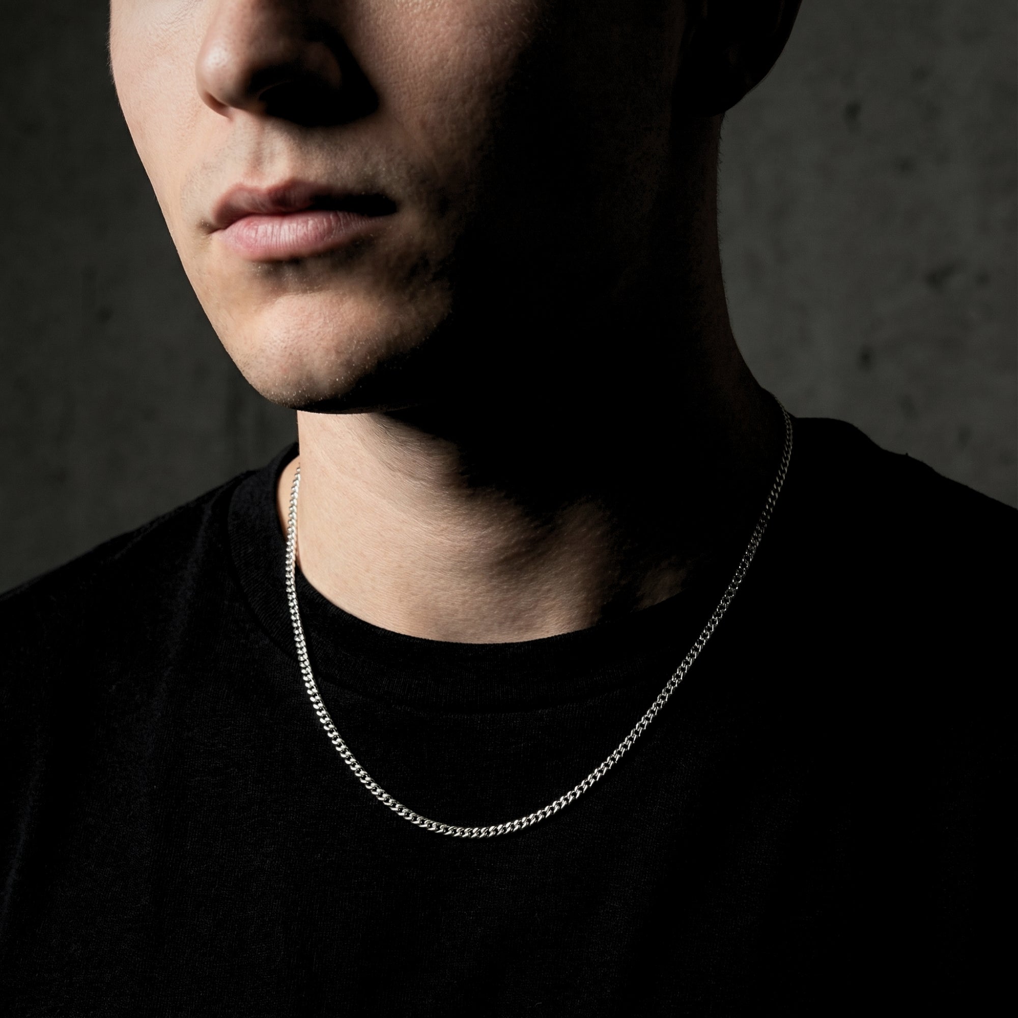 Male model wearing the slim 2mm silver stainless steel curb chain against a dark background.