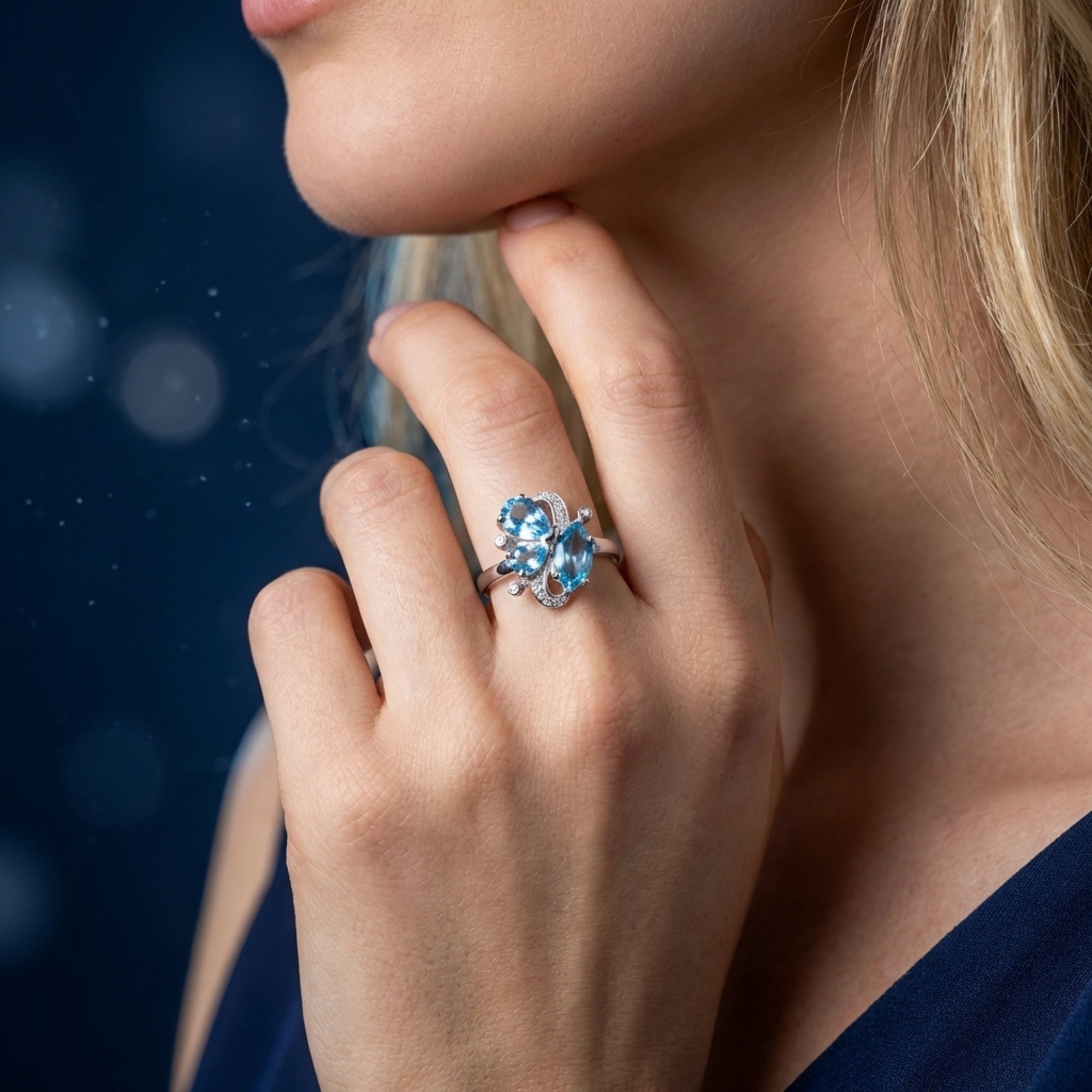 Silver Mariposa floral ring with blue topaz stones worn on a hand, styled with a dark blue dress.