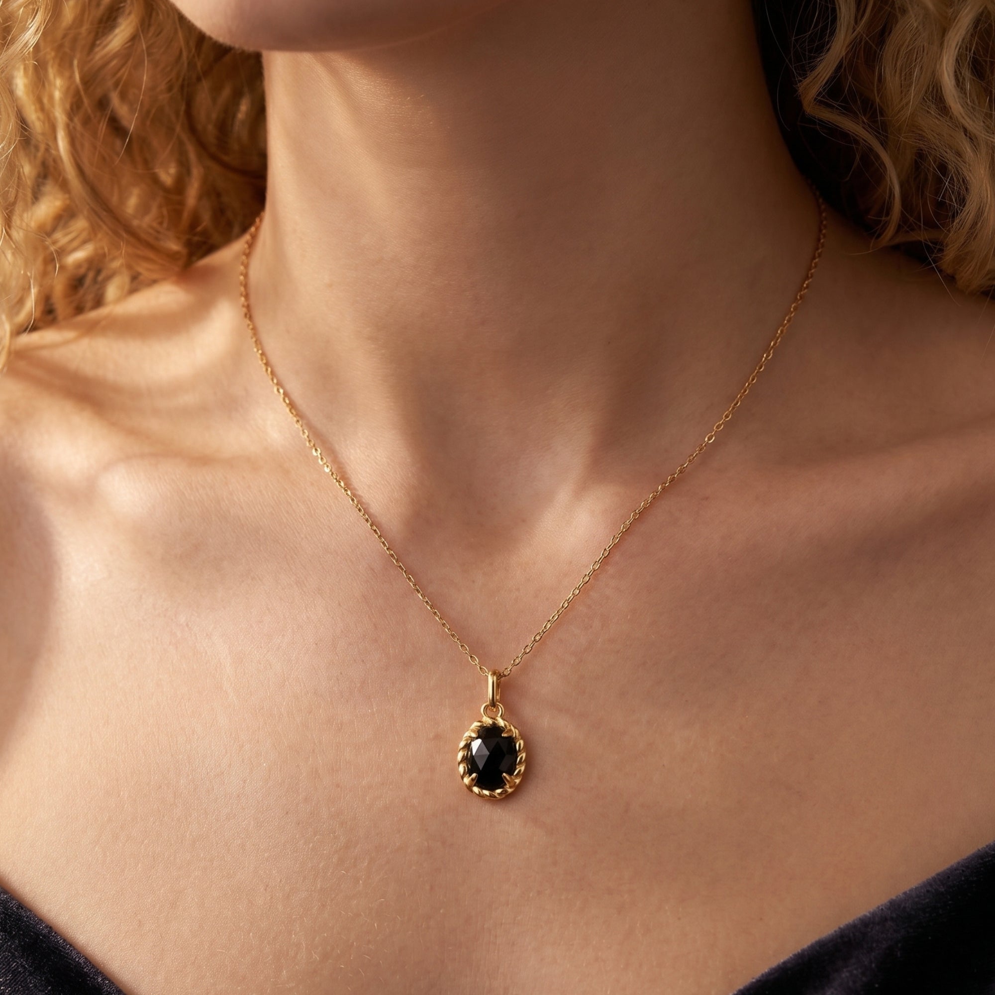 Close-up of a woman wearing a yellow gold necklace with a faceted oval black onyx pendant in a rope-textured setting.