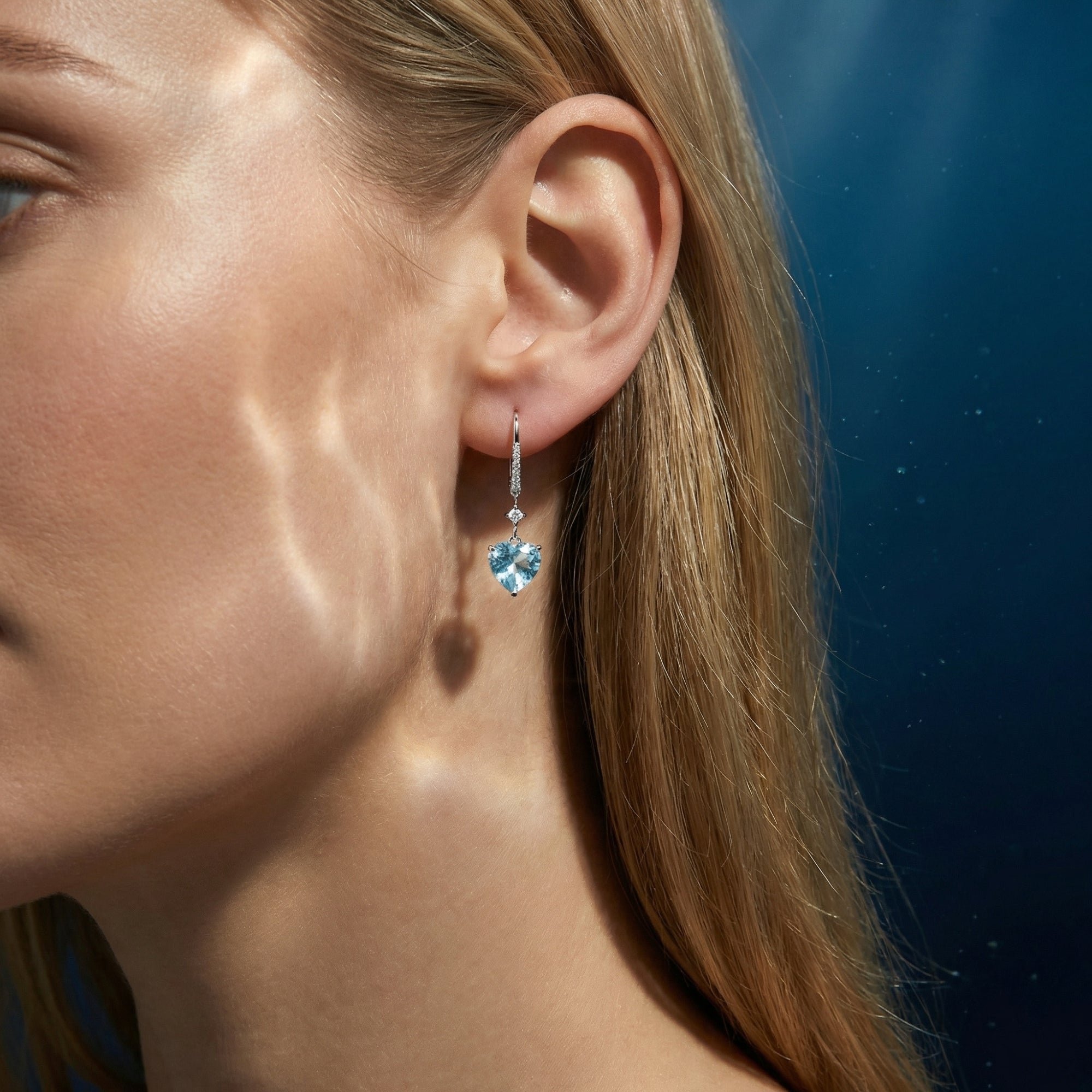 Side profile of a woman wearing a heart cut aquamarine and platinum drop earring with diamond accents.