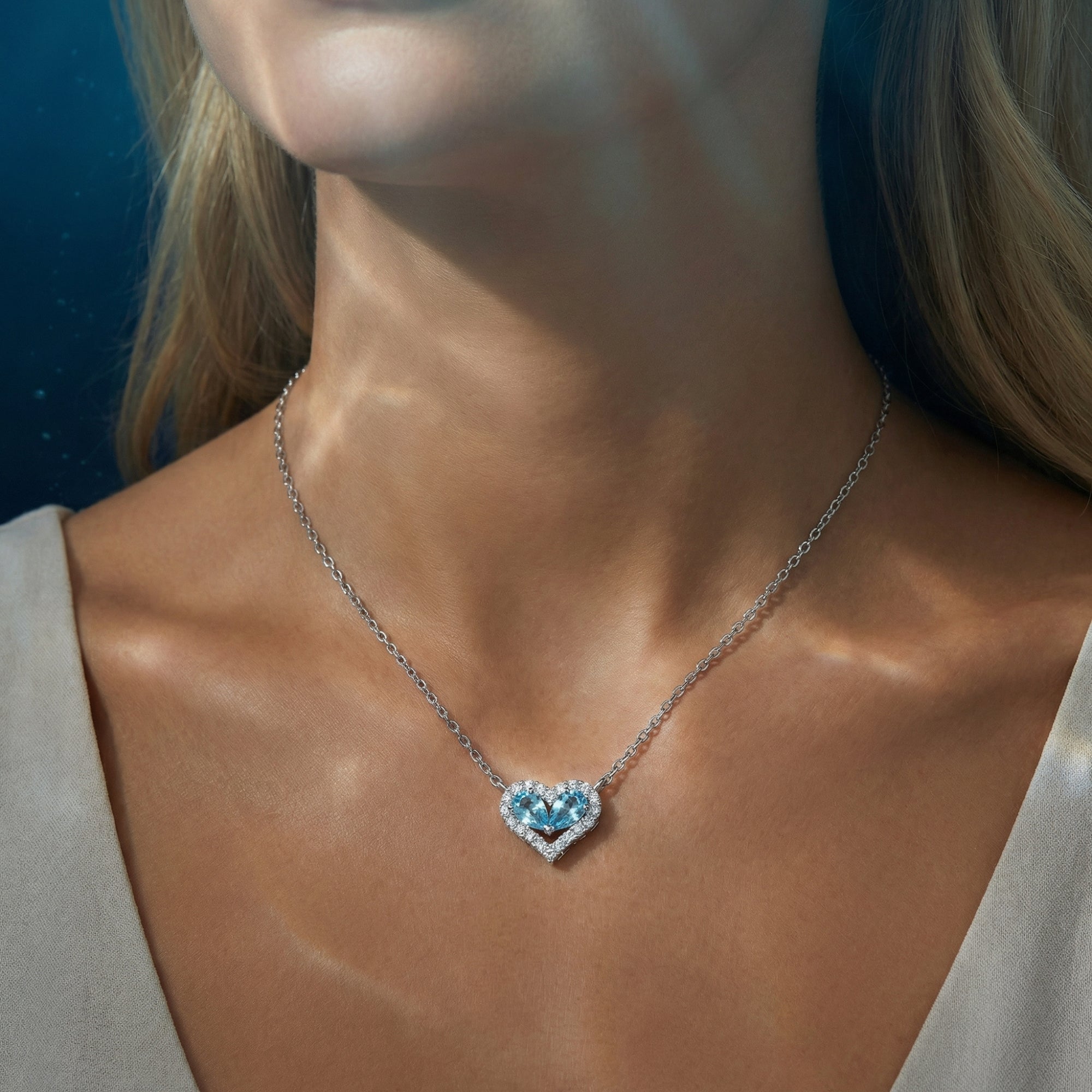 Close-up view of the silver heart-shaped aquamarine pendant necklace worn on a model's neck.
