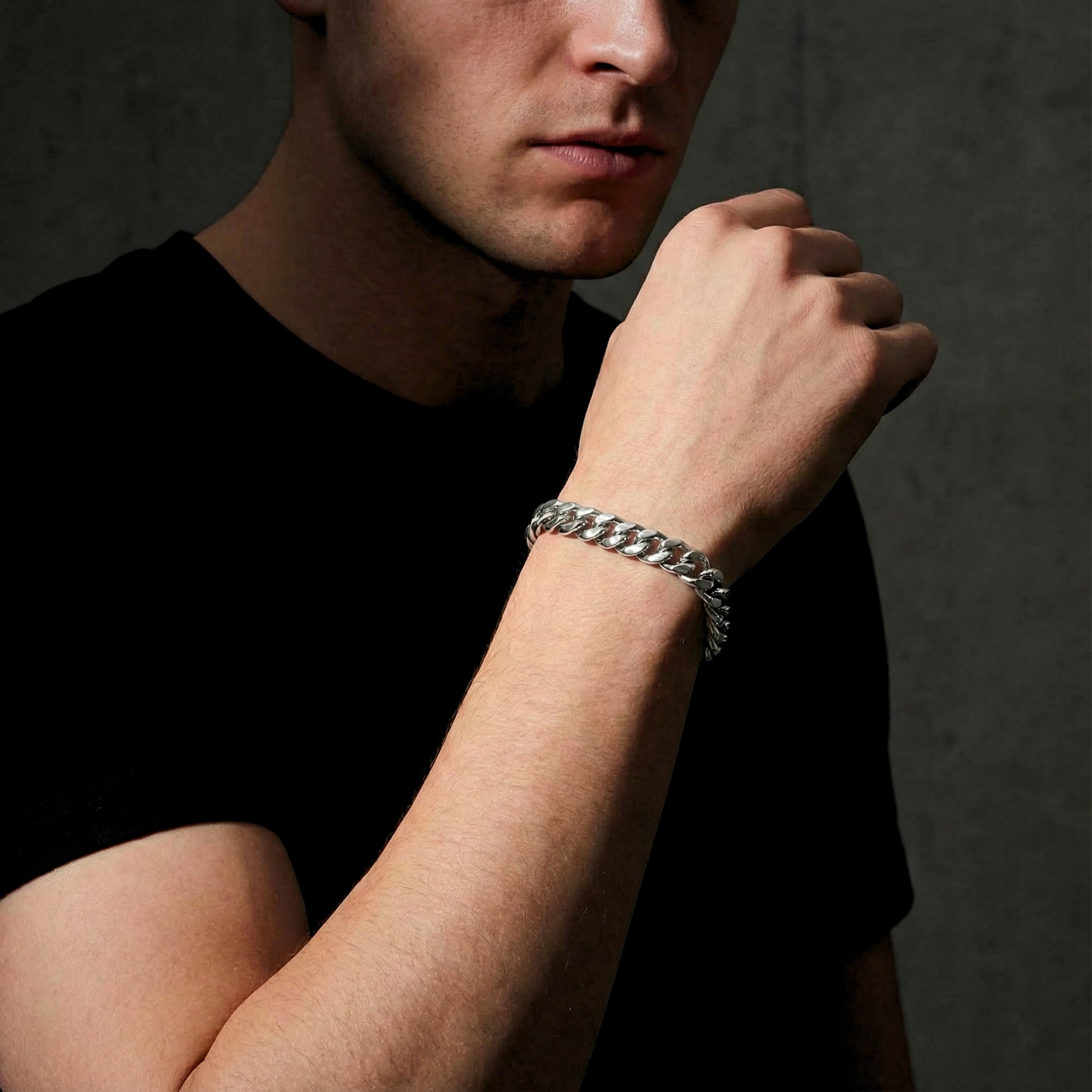 Silver stainless steel Cuban link bracelet for men shown on a model's wrist against a dark background.