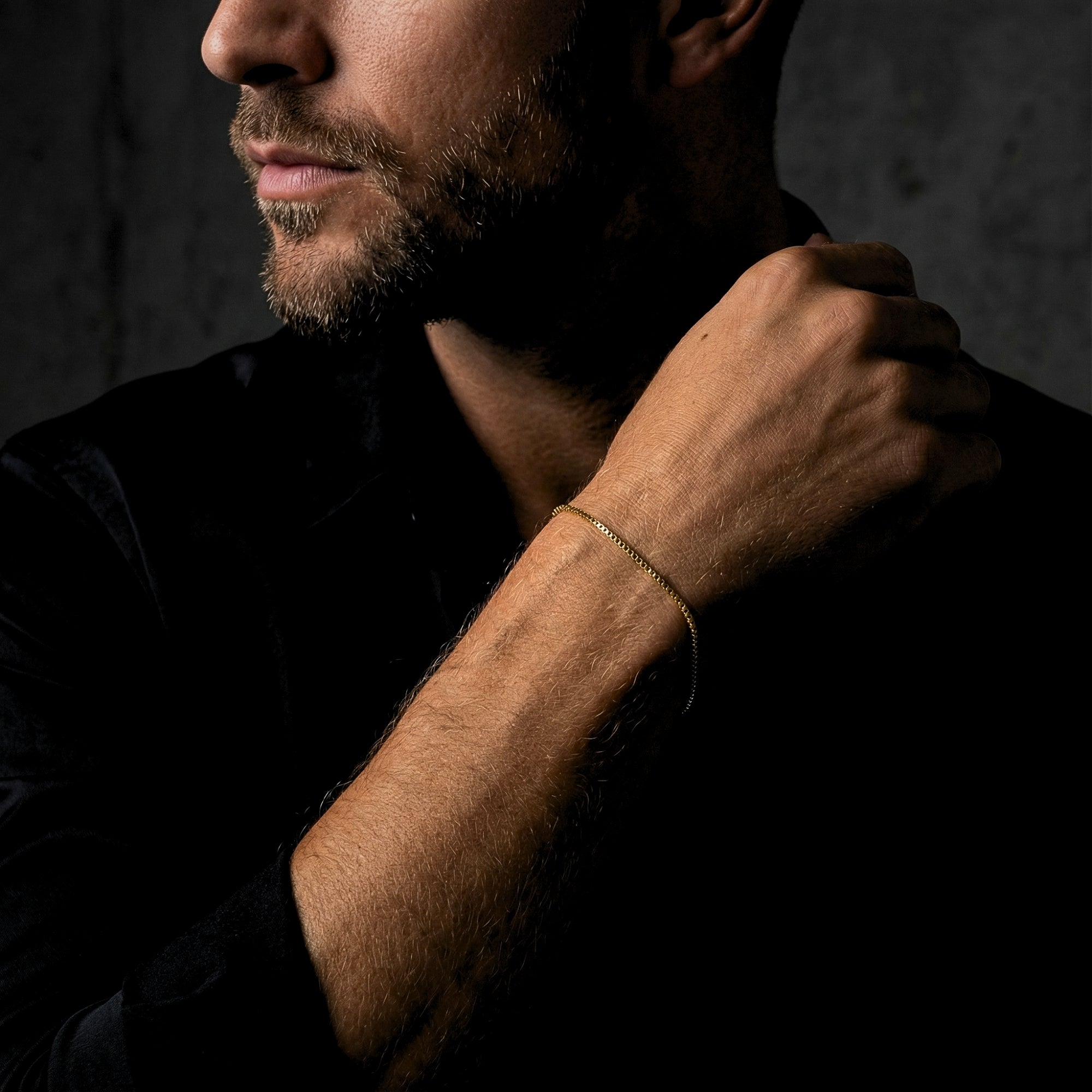 Side view of a man wearing a thin gold stainless steel box chain bracelet on his wrist.