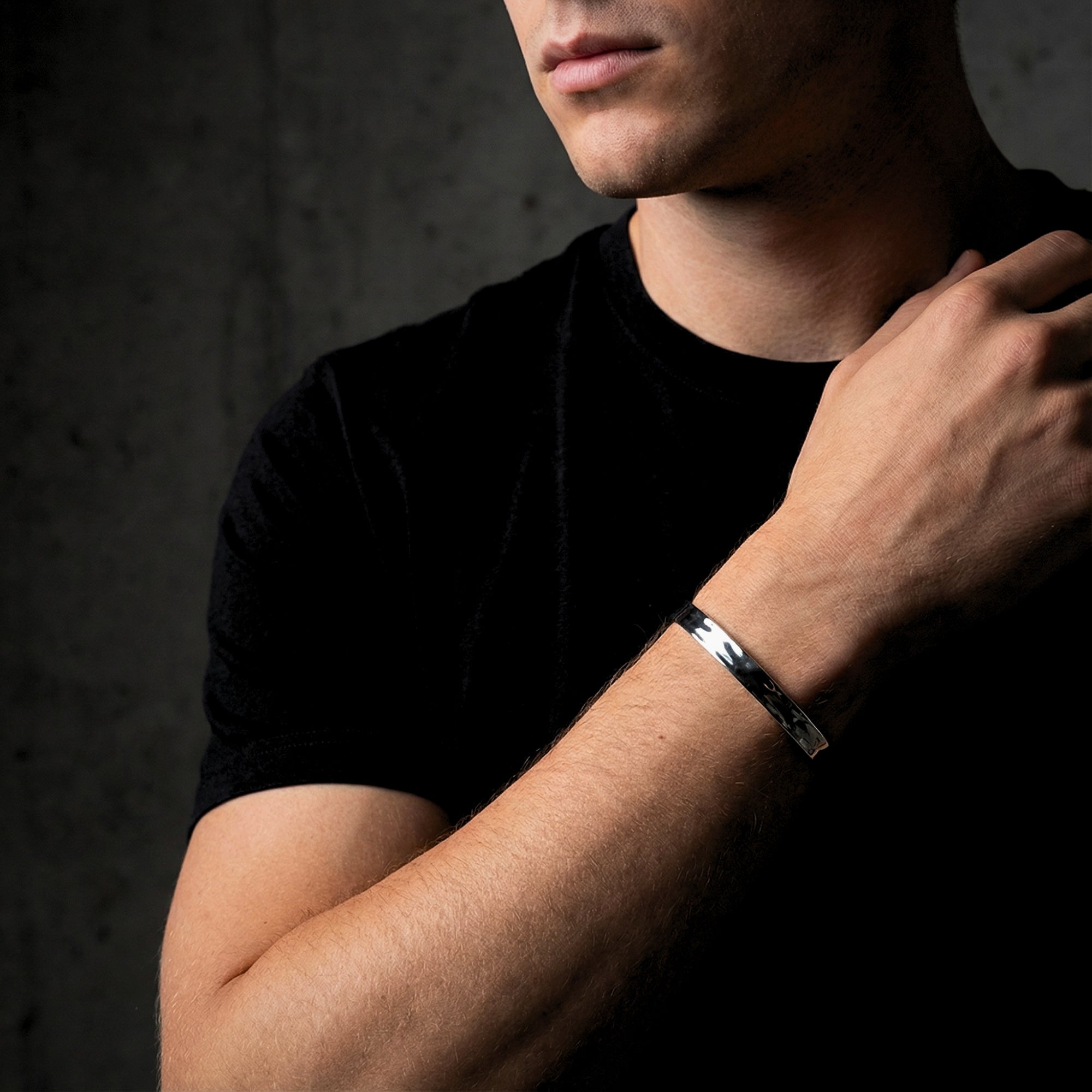 Silver hammered stainless steel cuff bangle for men worn by a model against a dark background.