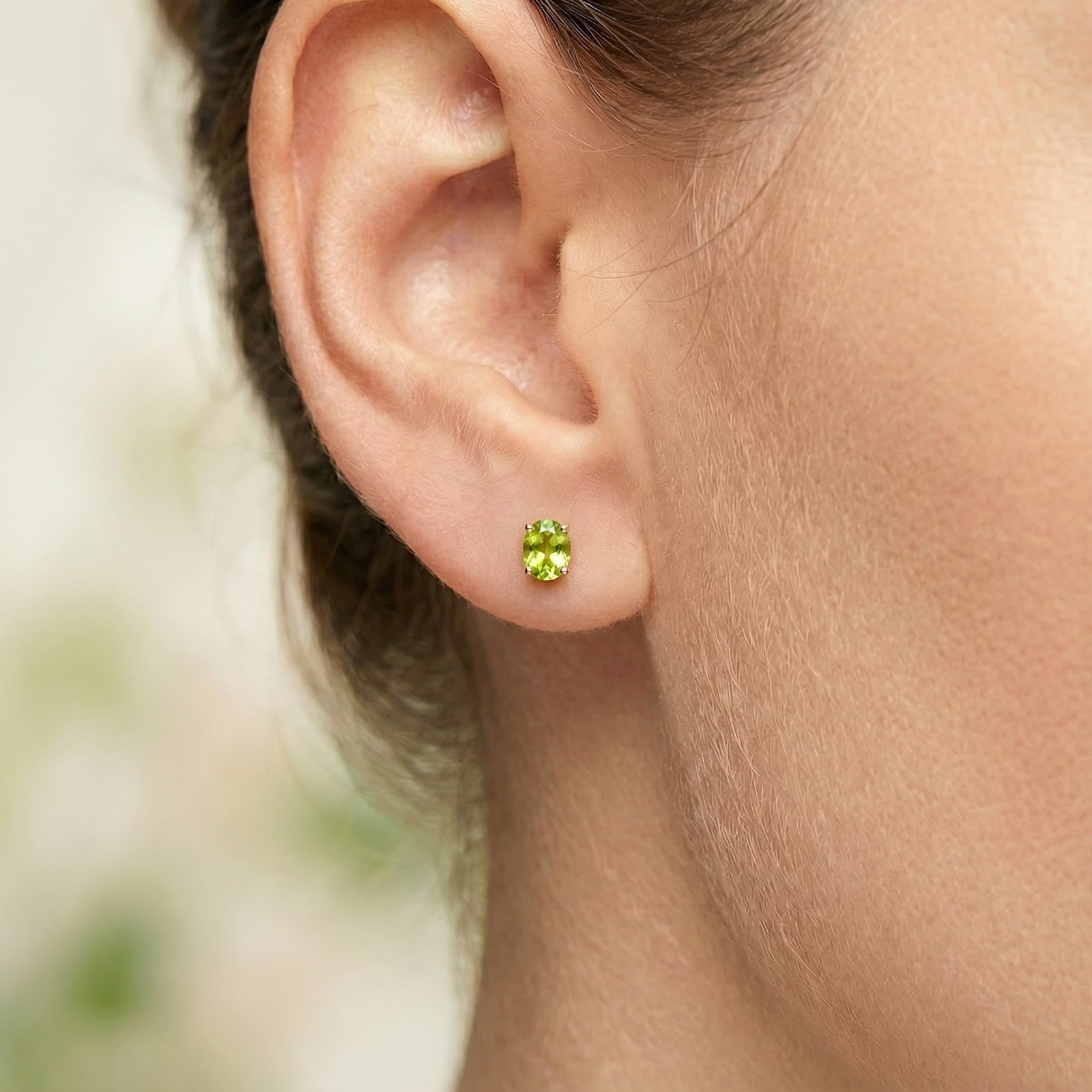 Close-up of an oval-cut simulated peridot stud earring in 18K gold vermeil worn on a model's ear.