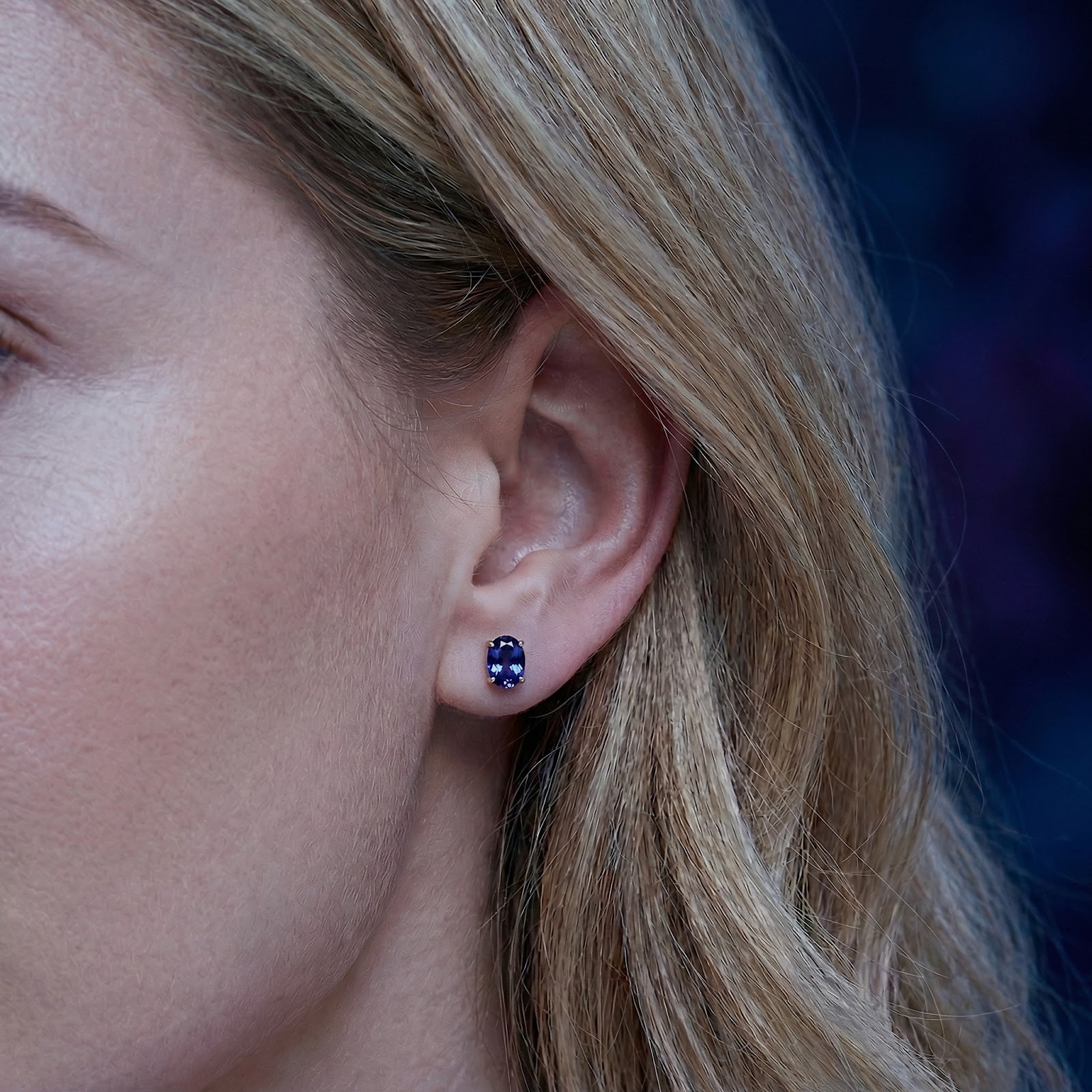 Woman wearing an oval cut simulated tanzanite stud earring in 18K gold vermeil on her earlobe.
