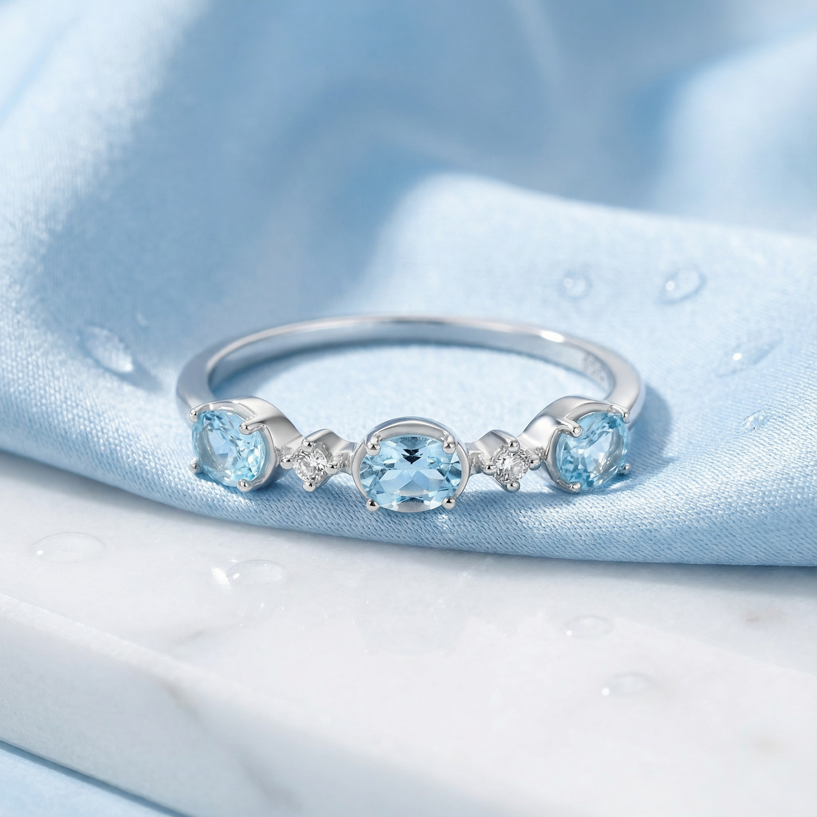 Maris bypass ring in S925 sterling silver with oval simulated aquamarines on blue silk and marble.