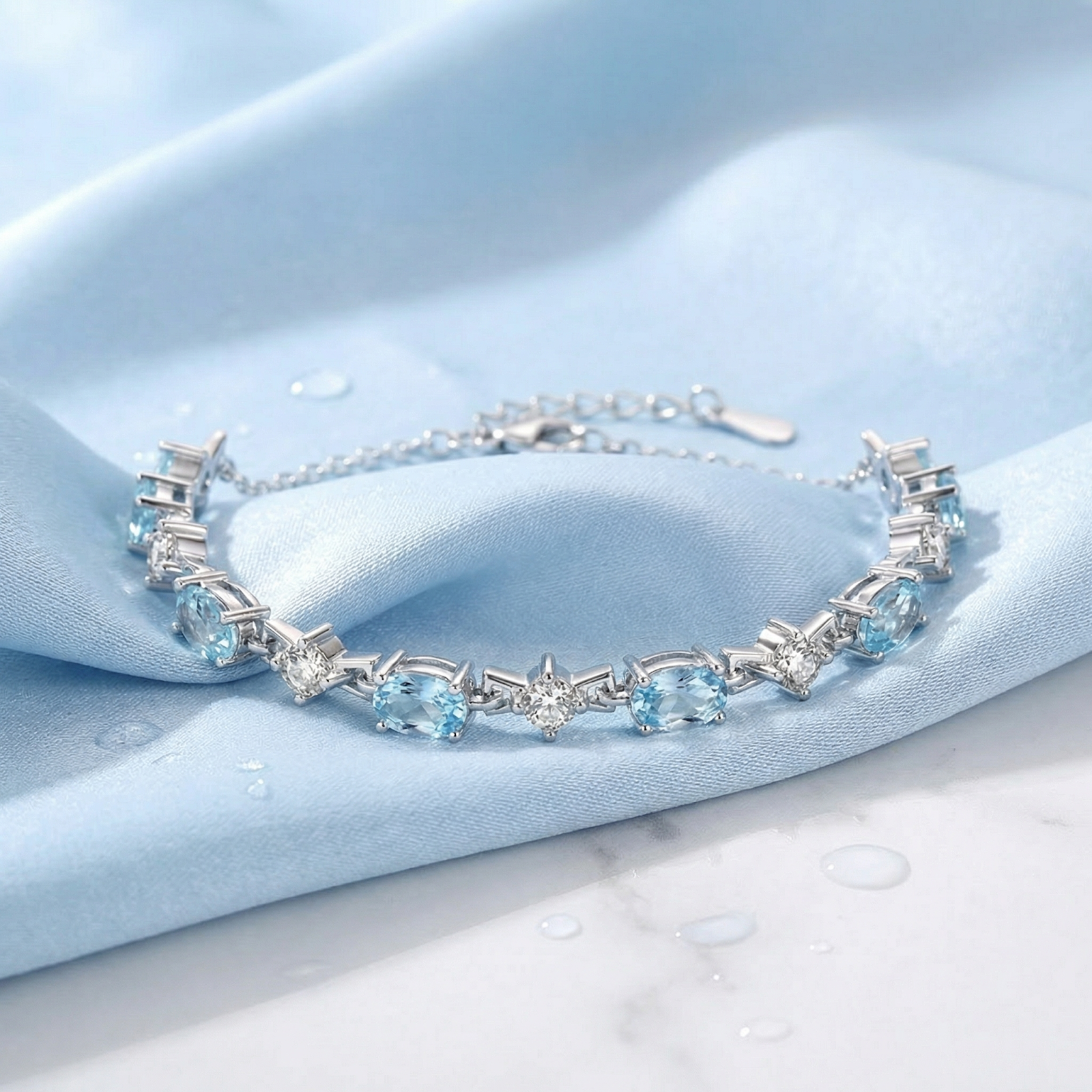 Sterling silver station bracelet with oval-cut light blue simulated aquamarine stones on blue silk fabric.