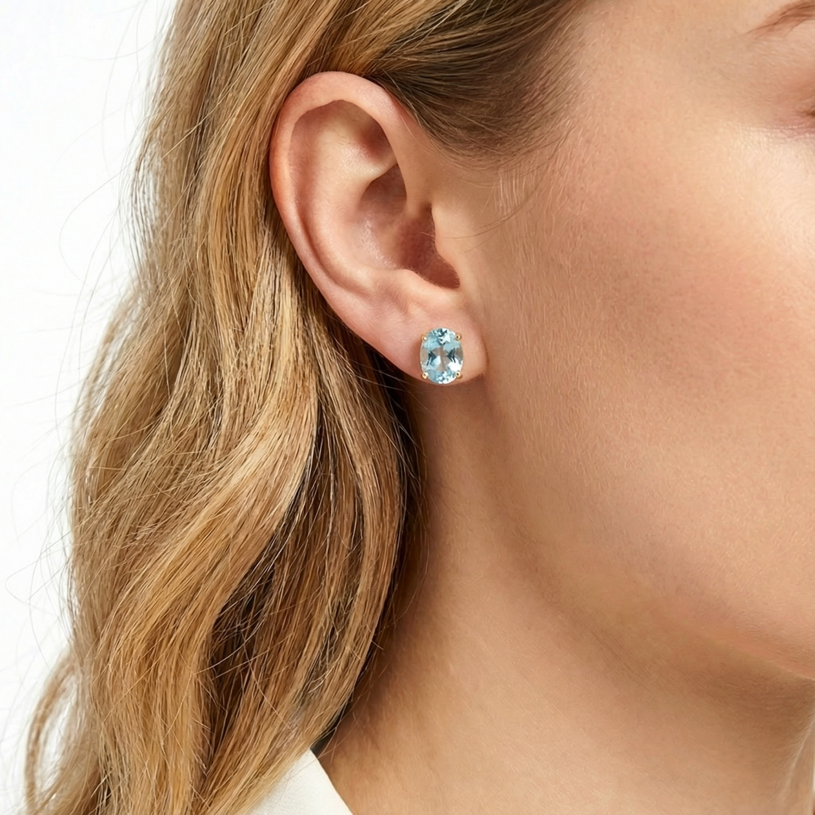 Woman wearing an emerald cut March birthstone simulated aquamarine stud earring in an 18K gold vermeil setting.
