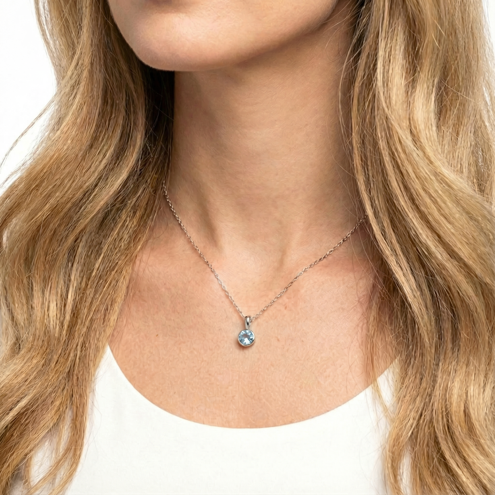 Close-up of the Marella sterling silver pendant with a round simulated aquamarine stone worn on a woman's neck.