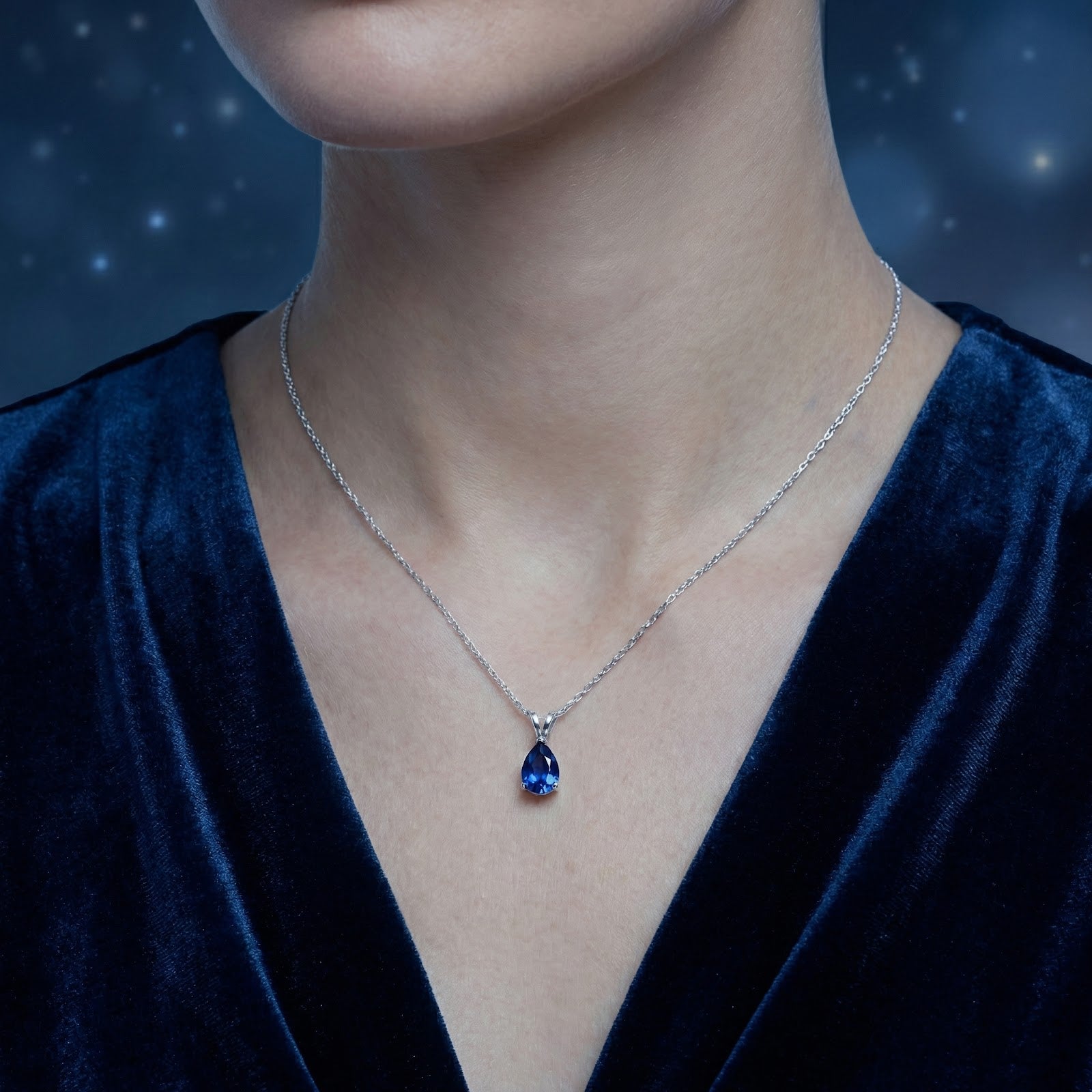 Model wearing the Thalyssa pear cut simulated sapphire necklace in sterling silver against a starry blue backdrop.