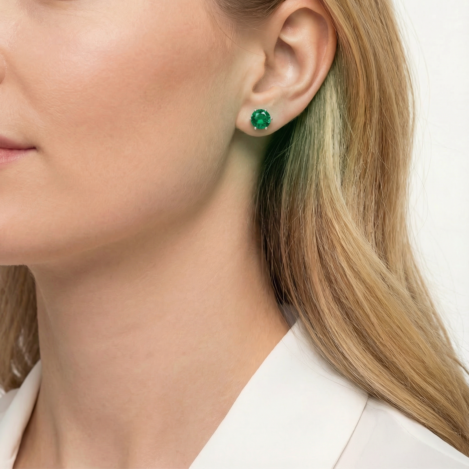 Side profile of a woman wearing a round cut simulated emerald stud earring in sterling silver.