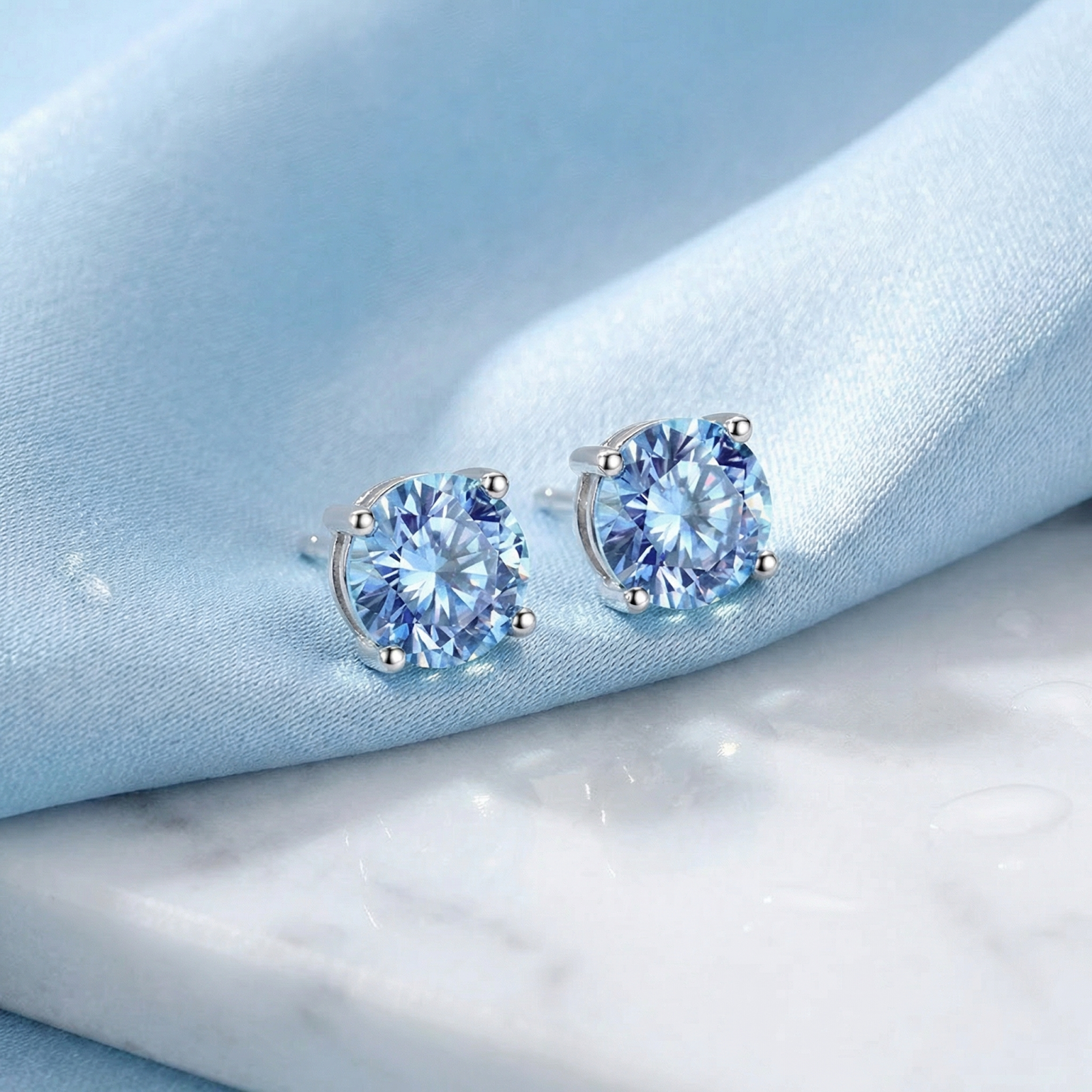 Angled view of round cut simulated aquamarine sterling silver stud earrings on blue silk and white marble.
