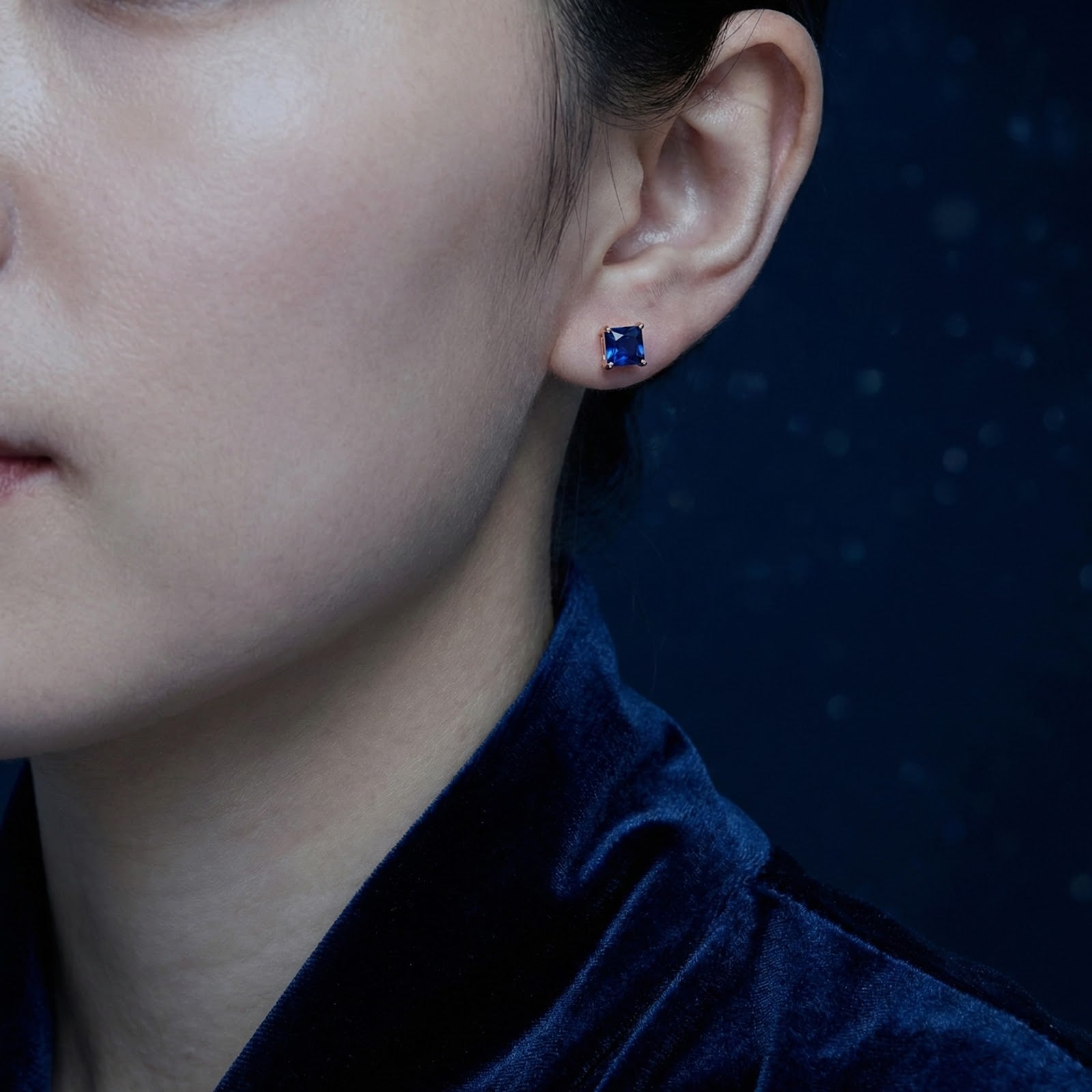 Square blue simulated sapphire stud earring in 18K rose gold vermeil shown on a model's ear.