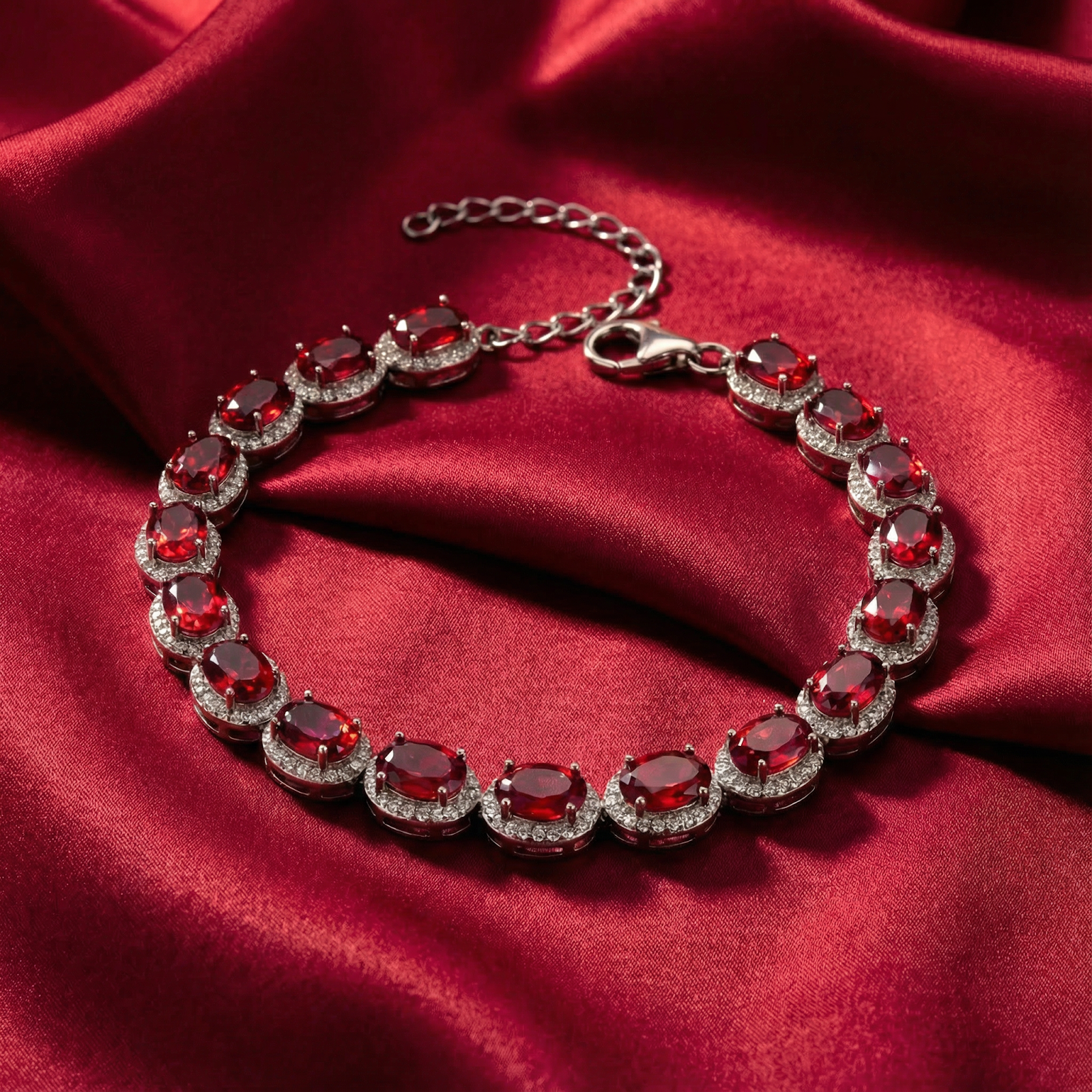 Oval-cut simulated ruby tennis bracelet in sterling silver displayed on red satin fabric.