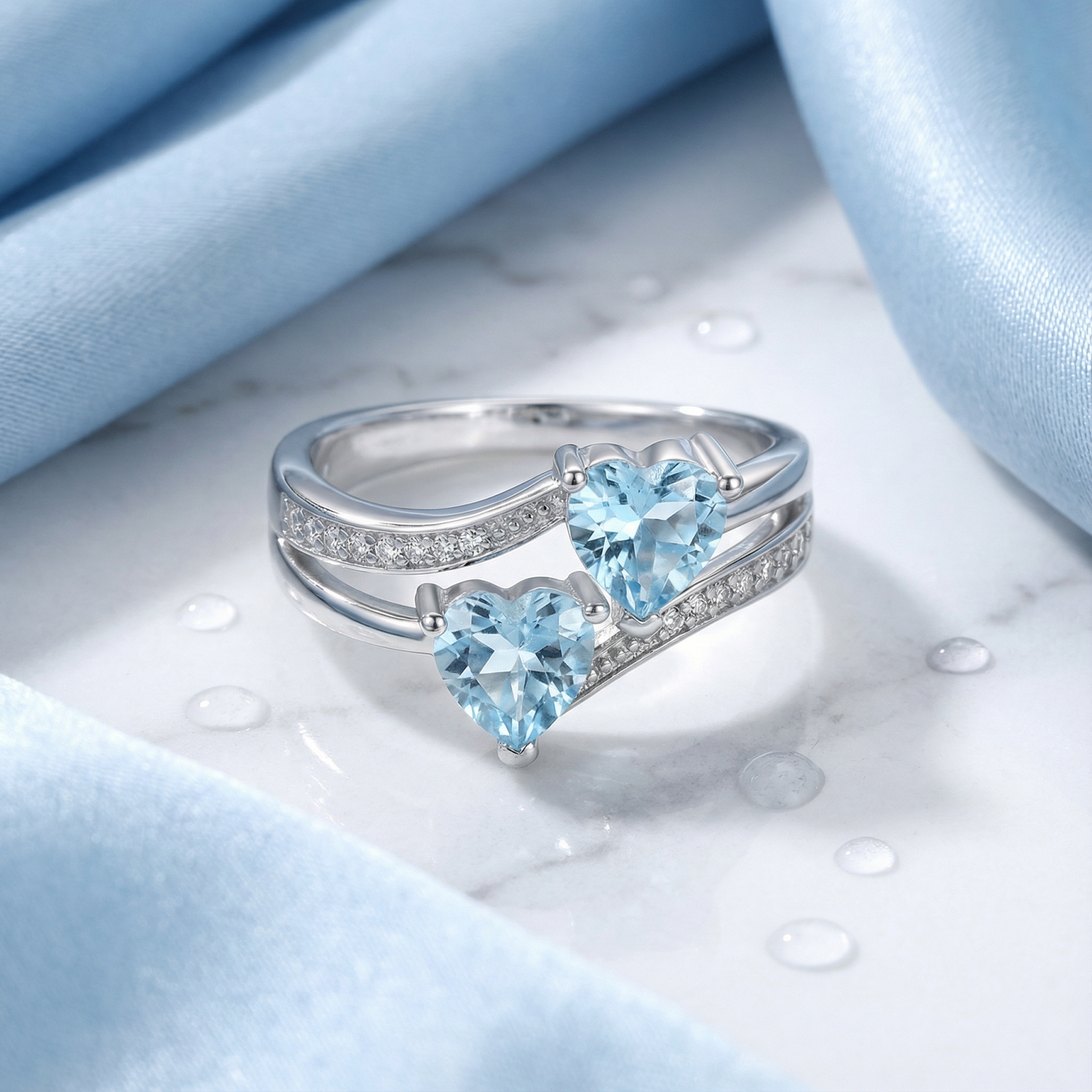 Heart-cut simulated aquamarine sterling silver bypass ring styled on a marble surface with blue silk fabric.