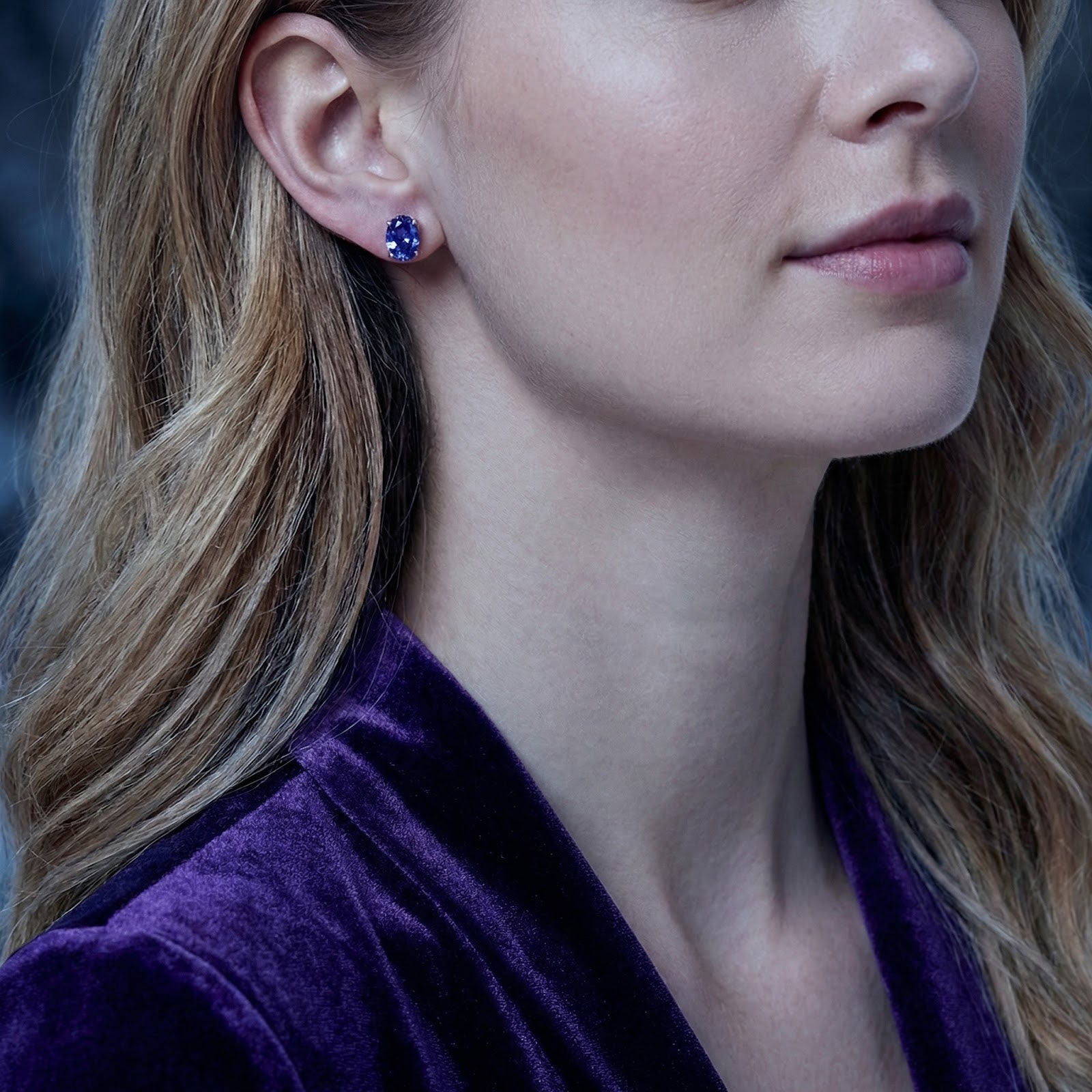 A woman wearing the Elianette oval simulated tanzanite stud earrings in sterling silver.