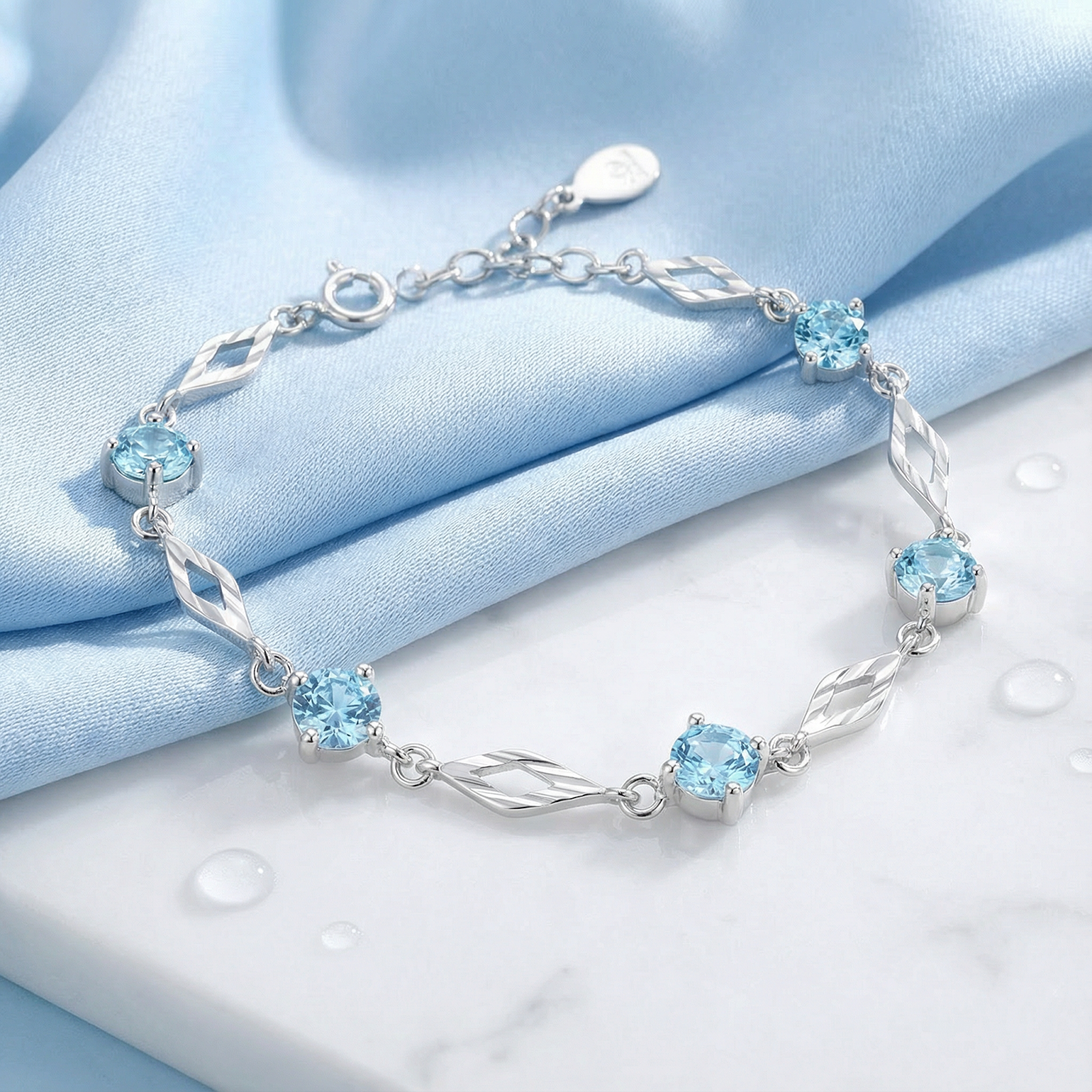 S925 sterling silver station bracelet featuring round simulated aquamarine stones on a blue silk background.