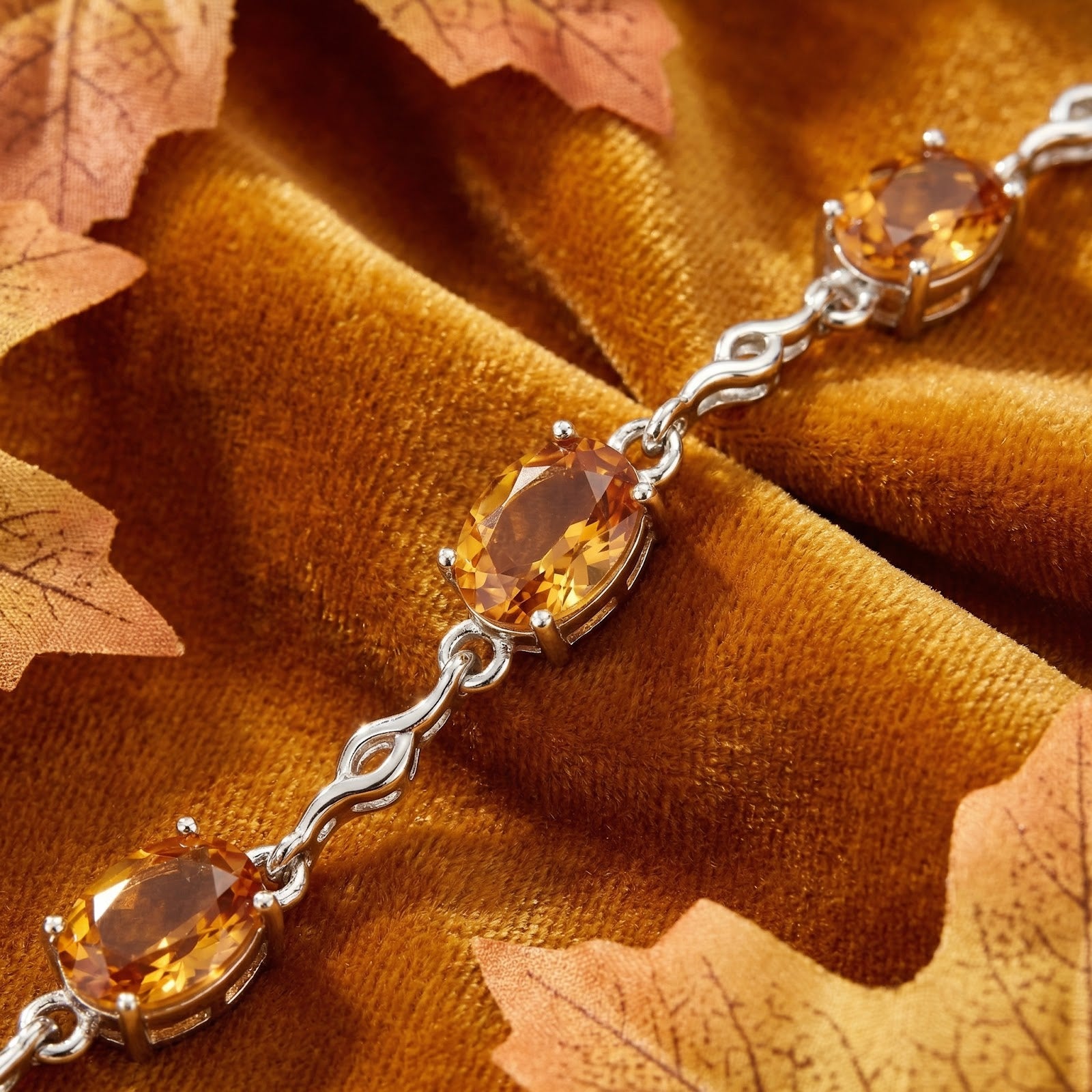Macro shot of oval-cut simulated topaz stones in a sterling silver link setting on brown velvet fabric.