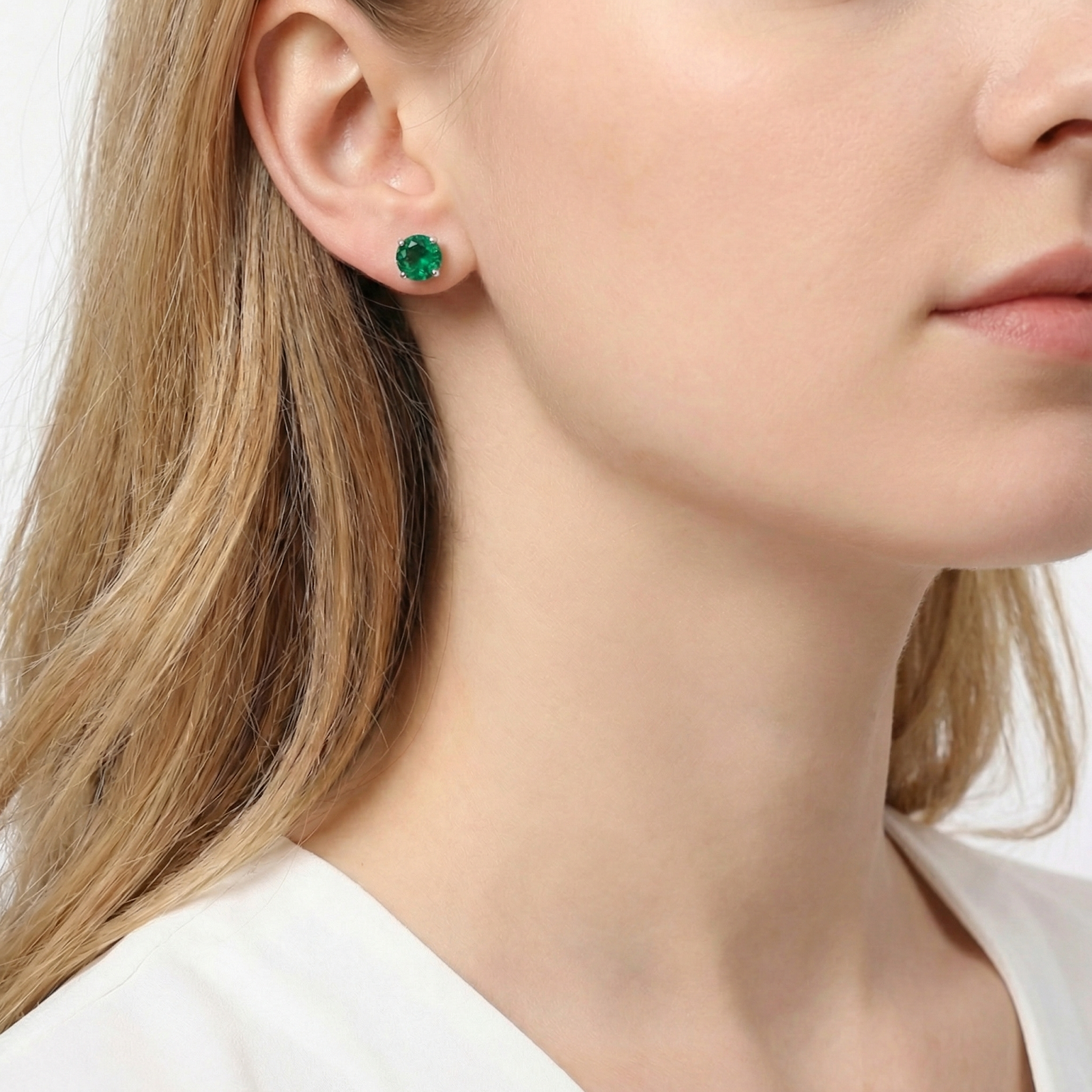 Woman wearing a round cut simulated emerald stud earring in sterling silver on her ear.