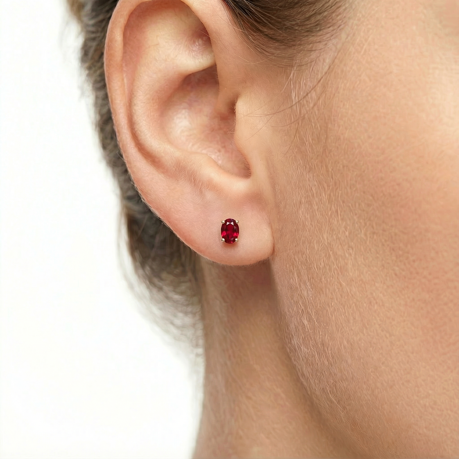 Close-up of an oval pigeon blood red simulated ruby earring in 18K gold vermeil worn on a model's ear.