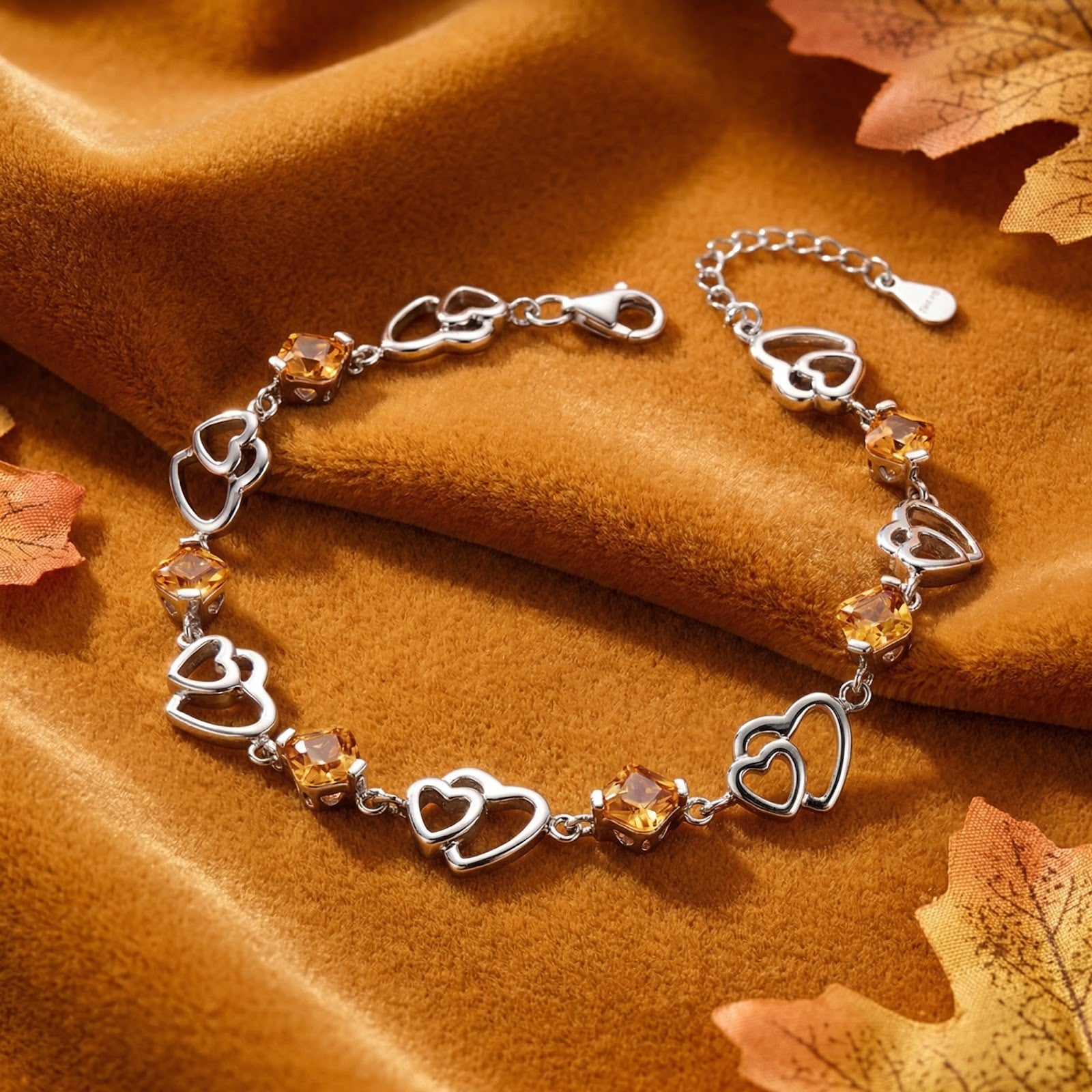 Sterling silver heart link bracelet with honeyed simulated topaz stones displayed on golden velvet with autumn leaves.