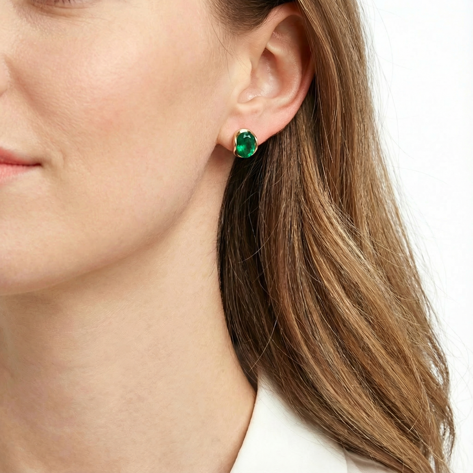 Profile view of a woman wearing The Veris Oval 18K gold plated simulated emerald earring.