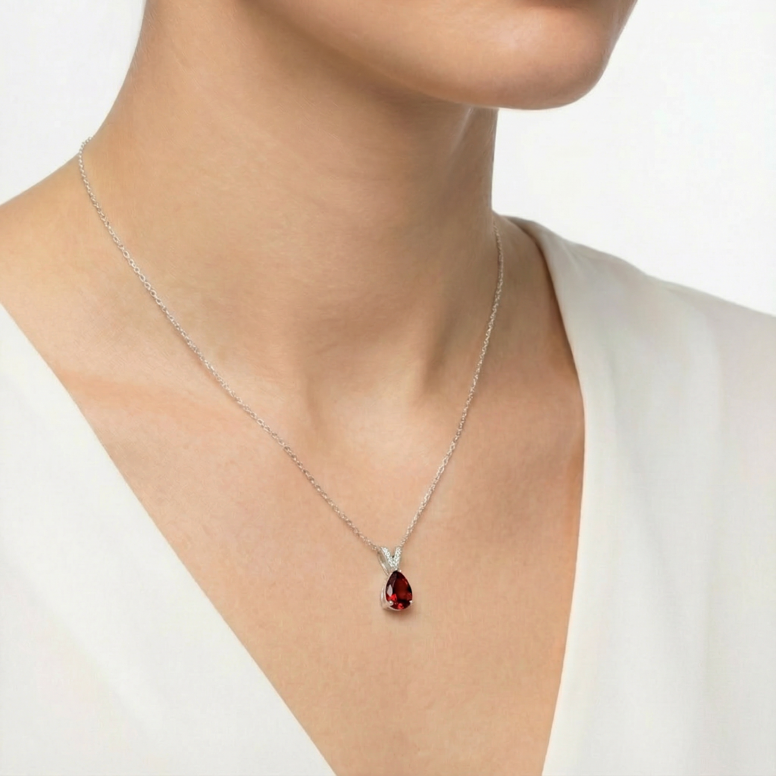 Sterling silver necklace with a pear cut simulated garnet pendant worn by a model in a white top.