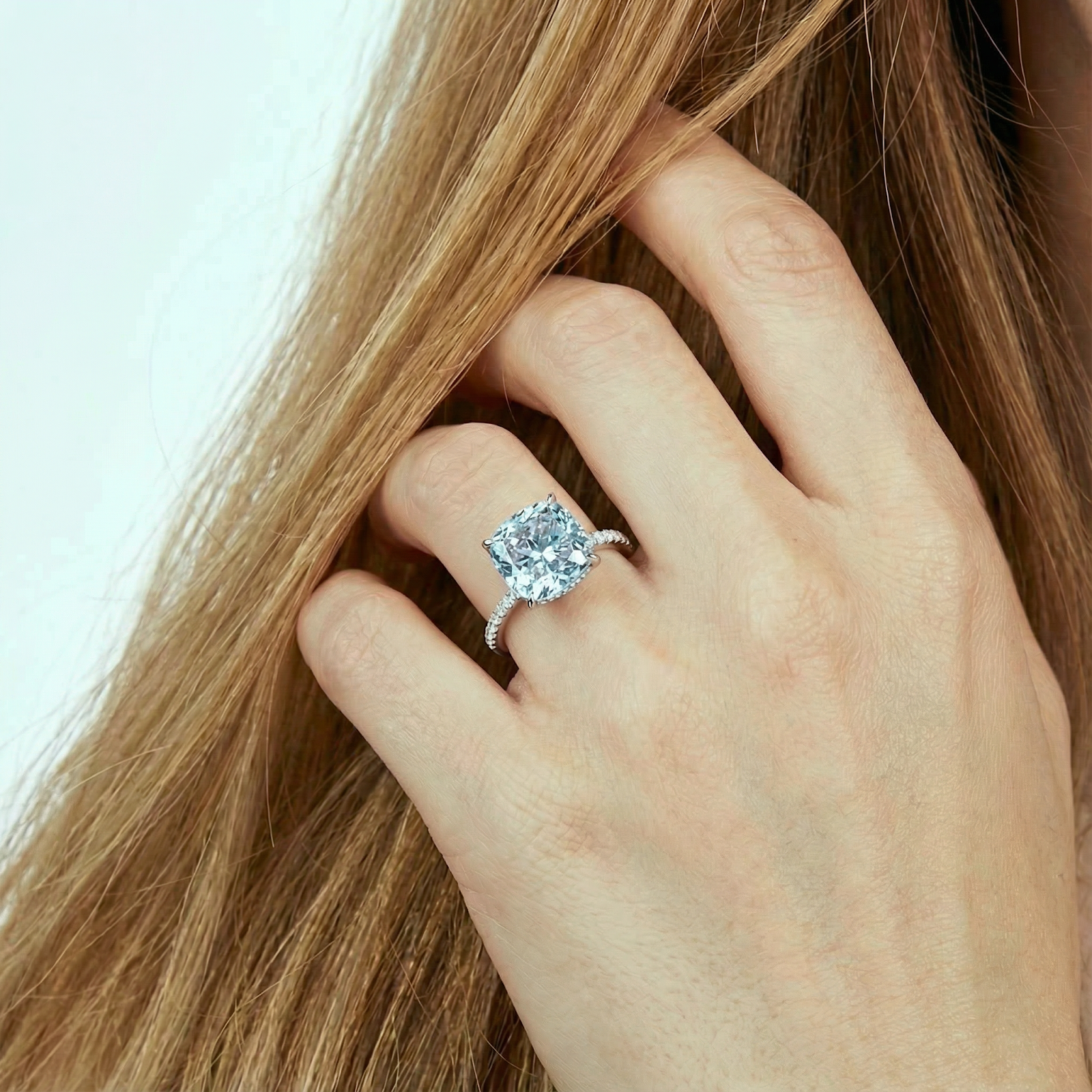 Cushion cut simulated aquamarine halo ring in S925 sterling silver worn on a finger against a backdrop of hair.