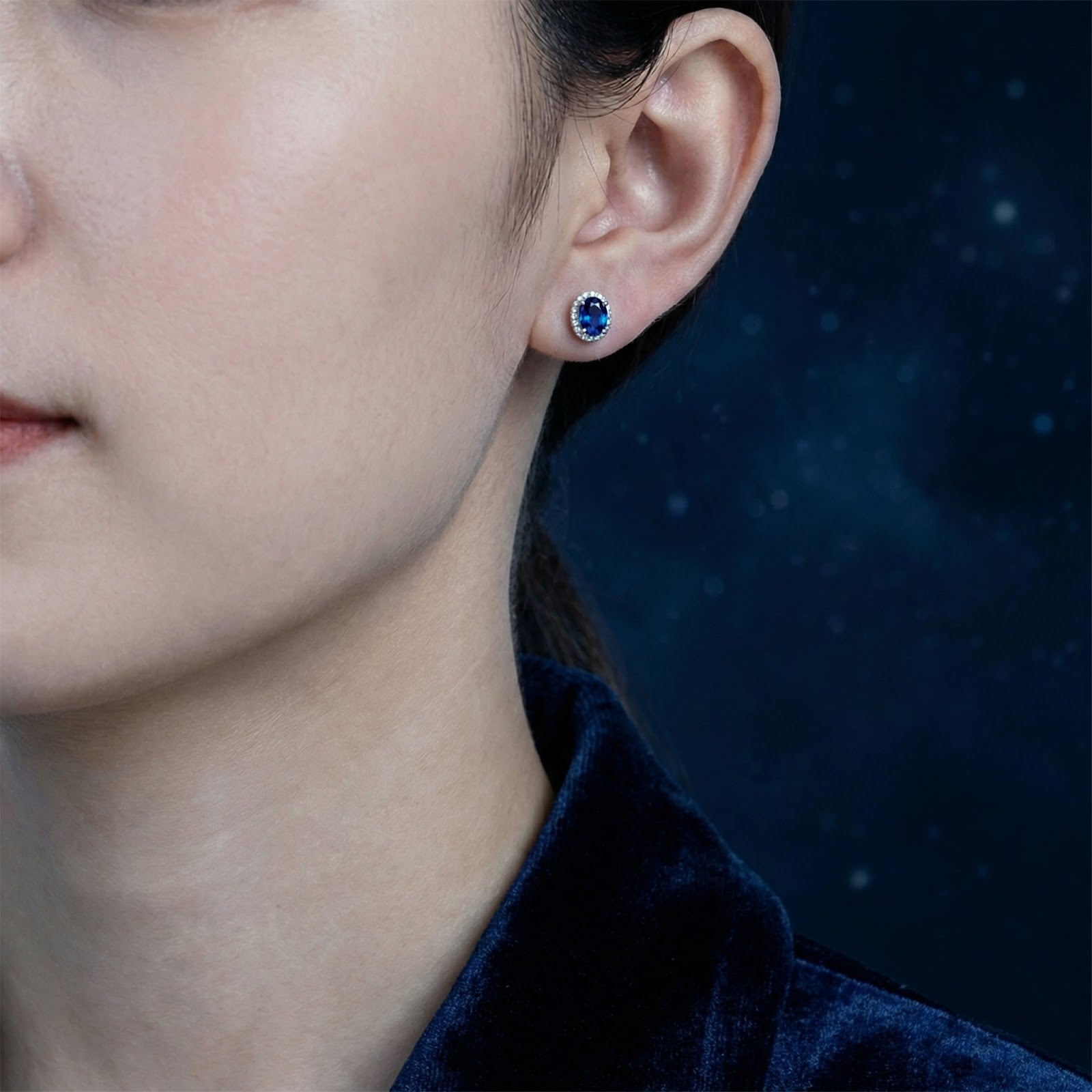 Woman wearing an oval simulated sapphire halo stud earring in sterling silver on her earlobe.
